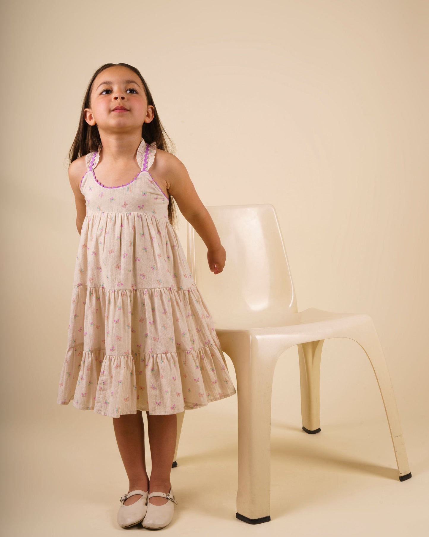Early Sunday, Laura Dress in Butterfly Print color, made from printed cotton tiny swiss dobby fabric, featuring Crisscross ruffle straps with delicate trim accents and a softly gathered tiered skirt, shown in a model standing facing front wearing