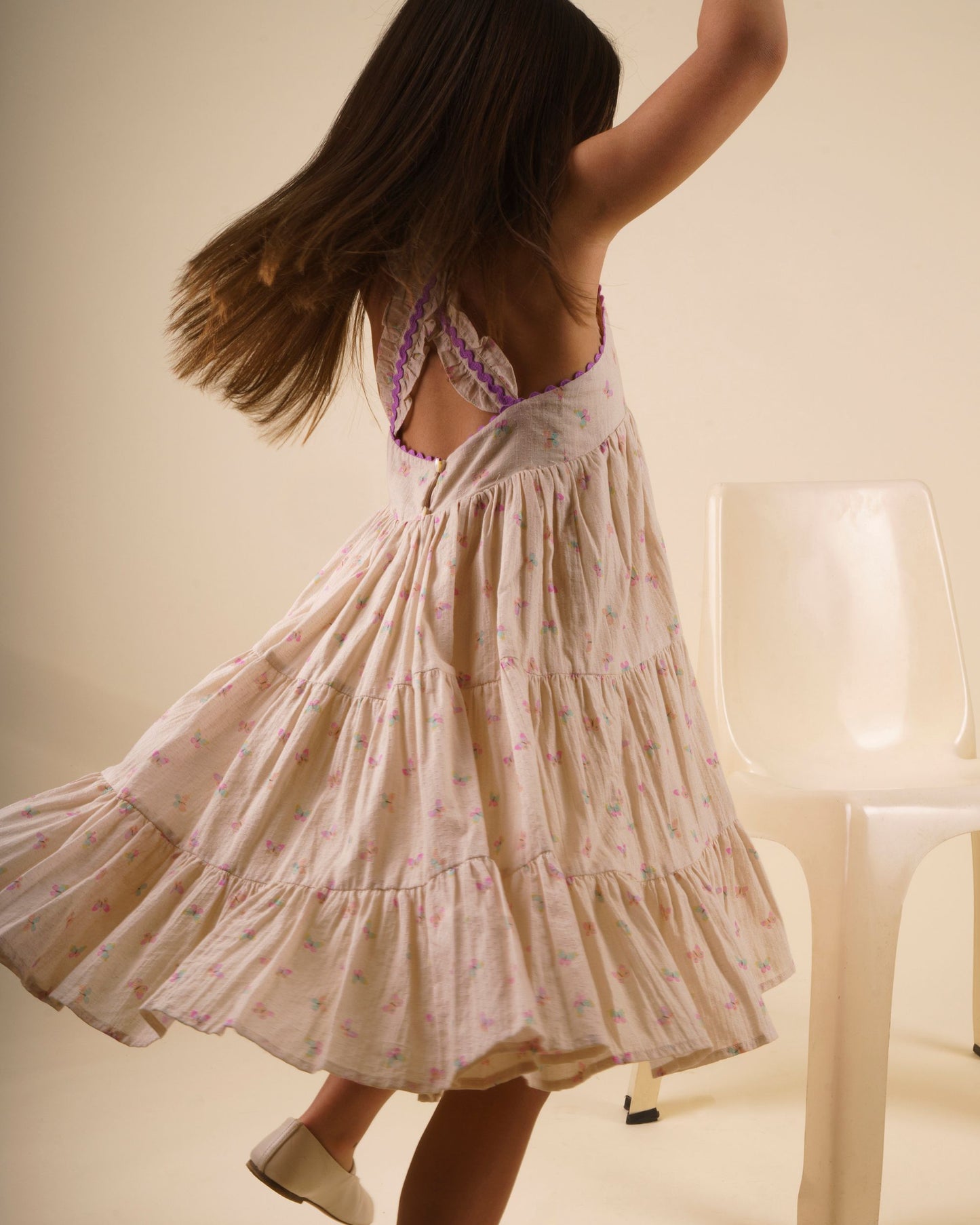 Early Sunday, Laura Dress in Butterfly Print color, made from printed cotton tiny swiss dobby fabric, featuring Crisscross ruffle straps with delicate trim accents and a softly gathered tiered skirt, shown in a Model walking / movement shot