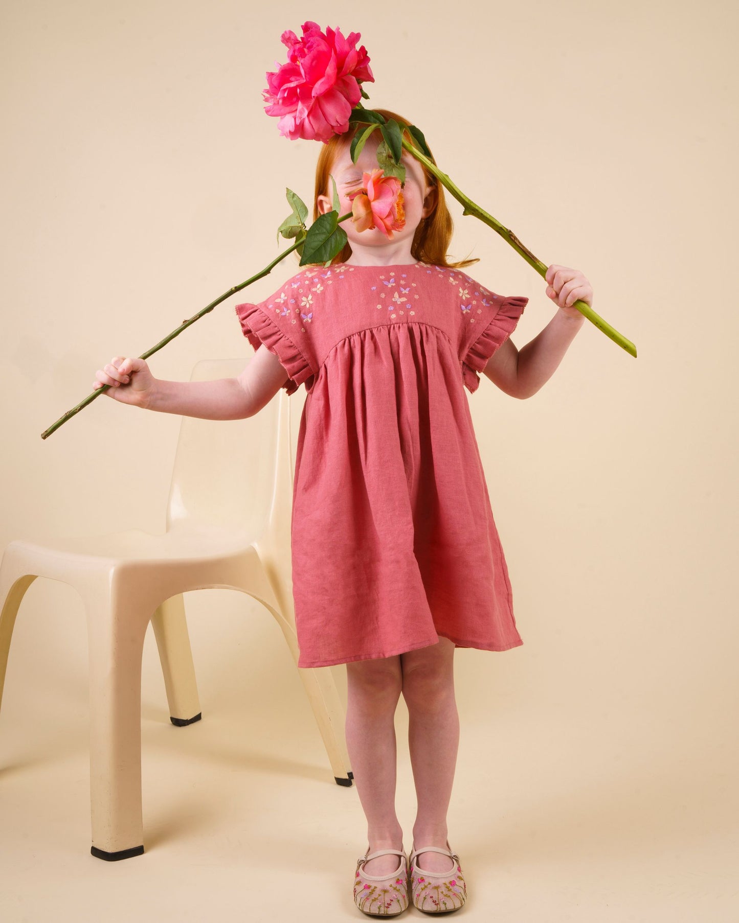 Early Sunday, Lila Dress in Peony color, made from 70% cotton 30% linen solid fabric, featuring Scalloped neckline with contrast stitching, flutter sleeves, gentle gathers, and embroidered hem detail, shown in a front view of model wearing it