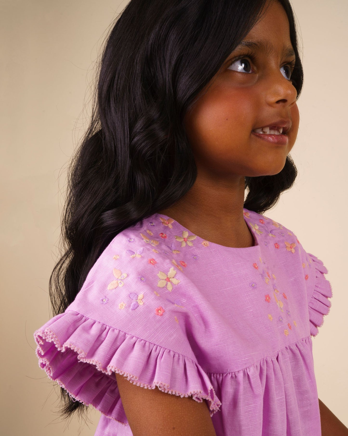 Early Sunday, Lila Dress in Lilac color, made from 70% cotton 30% linen solid fabric, featuring Scalloped neckline with contrast stitching, flutter sleeves, gentle gathers, and embroidered hem detail, shown in a close up shot of model wearing it