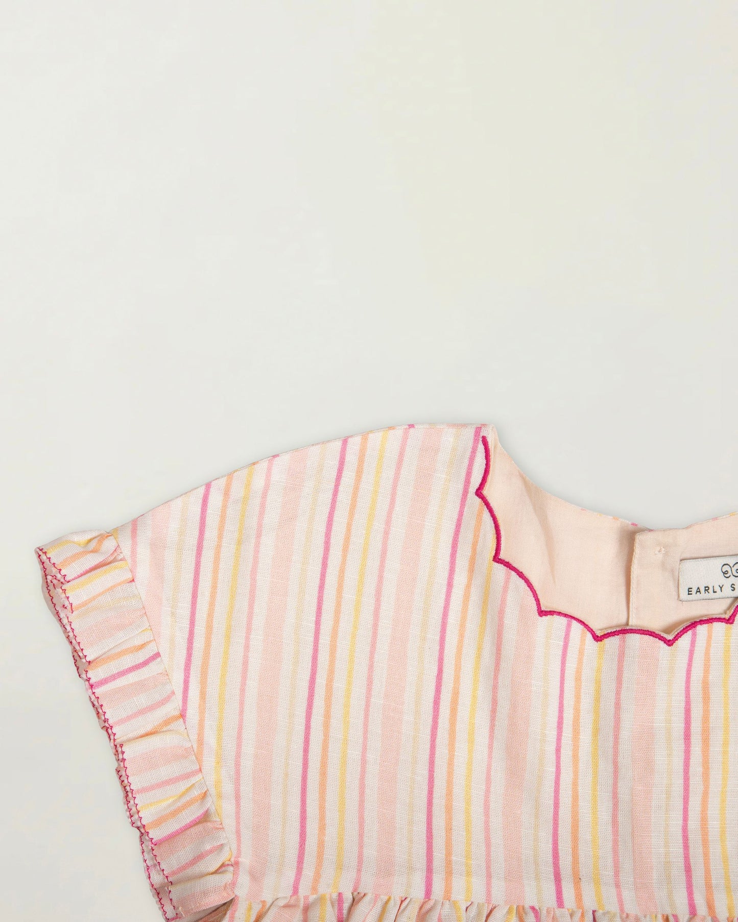 Early Sunday, Lila Dress in Pink Stripes color, made from printed 70% cotton 30% linen fabric, featuring Scalloped neckline with contrast stitching, flutter sleeves, gentle gathers, and embroidered hem detail, shown in a closeup flat-lay view