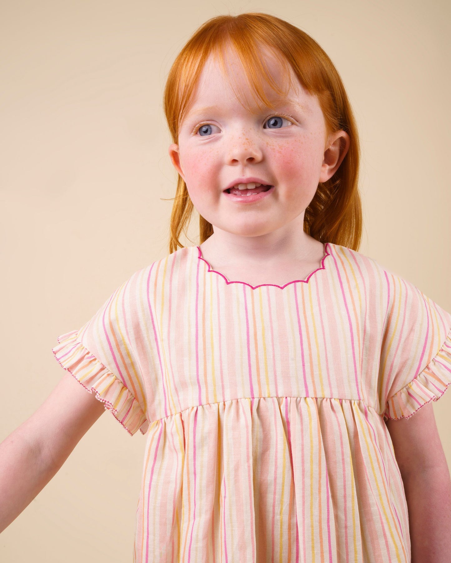 Early Sunday, Lila Dress in Pink Stripes color, made from printed 70% cotton 30% linen fabric, featuring Scalloped neckline with contrast stitching, flutter sleeves, gentle gathers, and embroidered hem detail, shown in a close-up of print