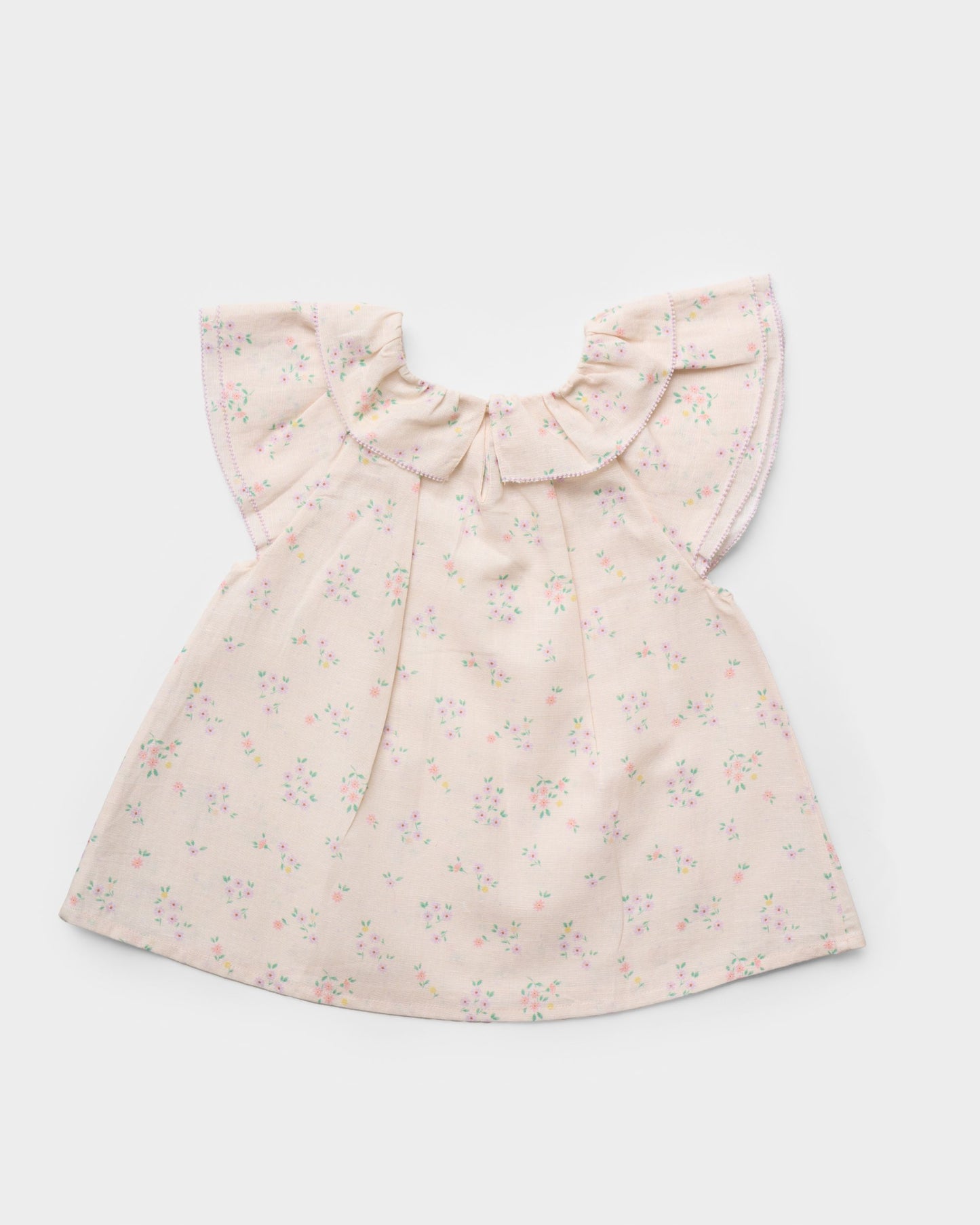 Early Sunday, Lola Blouse in Painted Bouquet color, made from printed 70% cotton 30% linen fabric, featuring Ruffled neckline, flutter sleeves with contrast detailing, and gentle gathers for a sweet silhouette, shown in a back flat-lay view