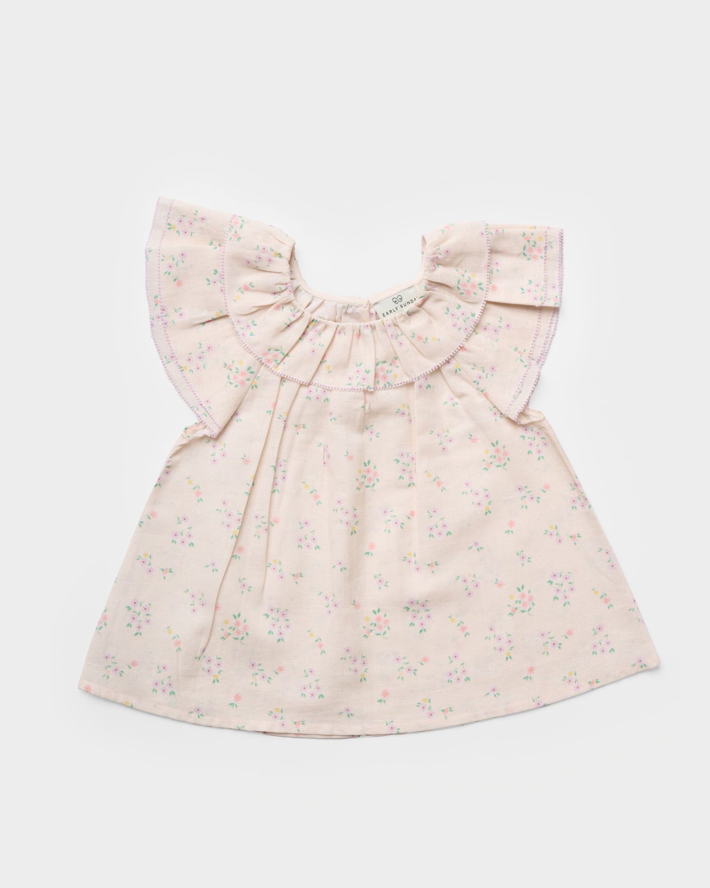 Early Sunday, Lola Blouse in Painted Bouquet color, made from printed 70% cotton 30% linen fabric, featuring Ruffled neckline, flutter sleeves with contrast detailing, and gentle gathers for a sweet silhouette, shown in a front flat-lay view