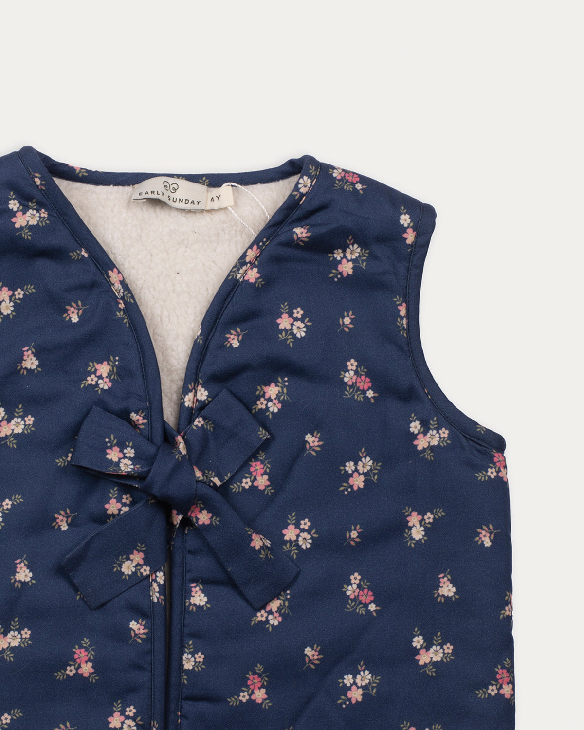 Early Sunday, Lou Vest jacket in Ditsy Bouquet Navy, made from Printed Cotton Satin fabric, featuring sleeveless quilted silhouette with tie-up bow detailing, shown in a closeup flat-lay view