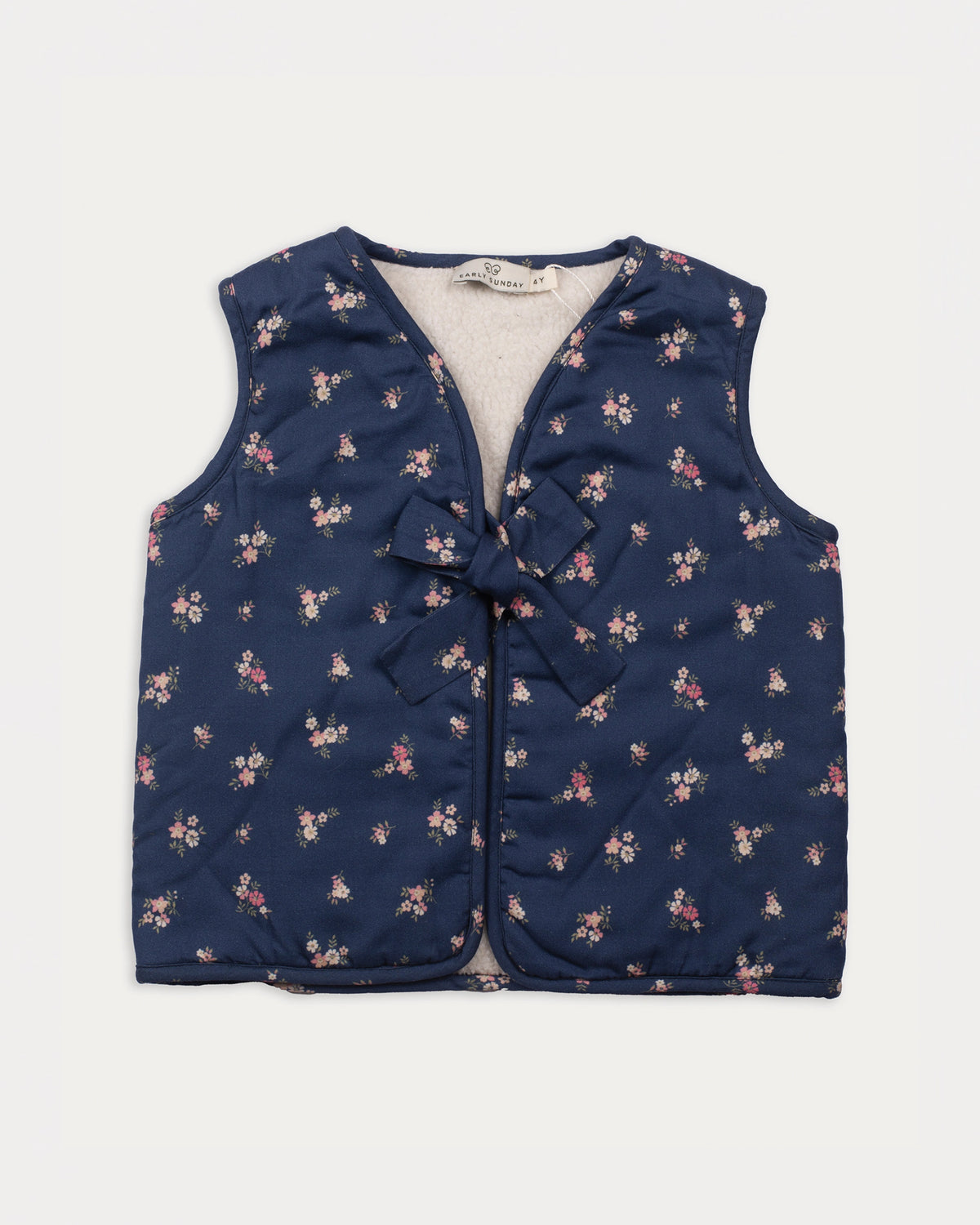 Early Sunday, Lou Vest jacket in Ditsy Bouquet Navy, made from Printed Cotton Satin fabric, featuring sleeveless quilted silhouette with tie-up bow detailing, shown in a front flat-lay view
