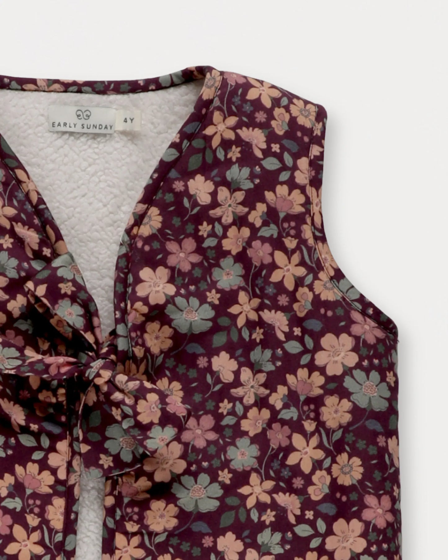 Early Sunday, Lou Vest jacket in Plum, made from Printed Cotton Satin fabric, featuring sleeveless quilted silhouette with tie-up bow detailing, shown in a closeup flat-lay view