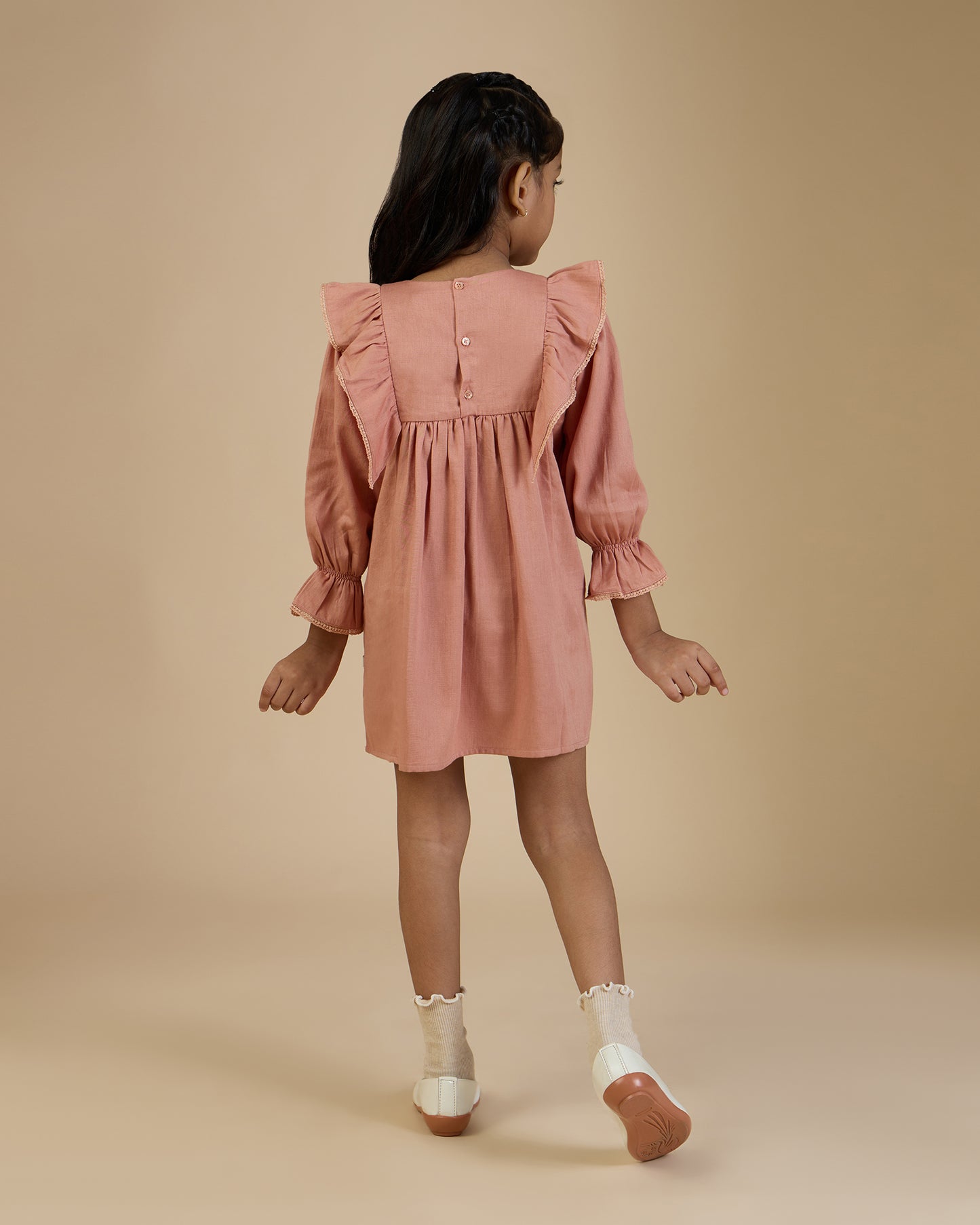 Early Sunday, Margot Dress in Earthy Pink, made from Cotton Satin fabric, featuring classic silhouette with floral embroidery around the yoke and ruffle detailing, shown in a back view of model wearing it
