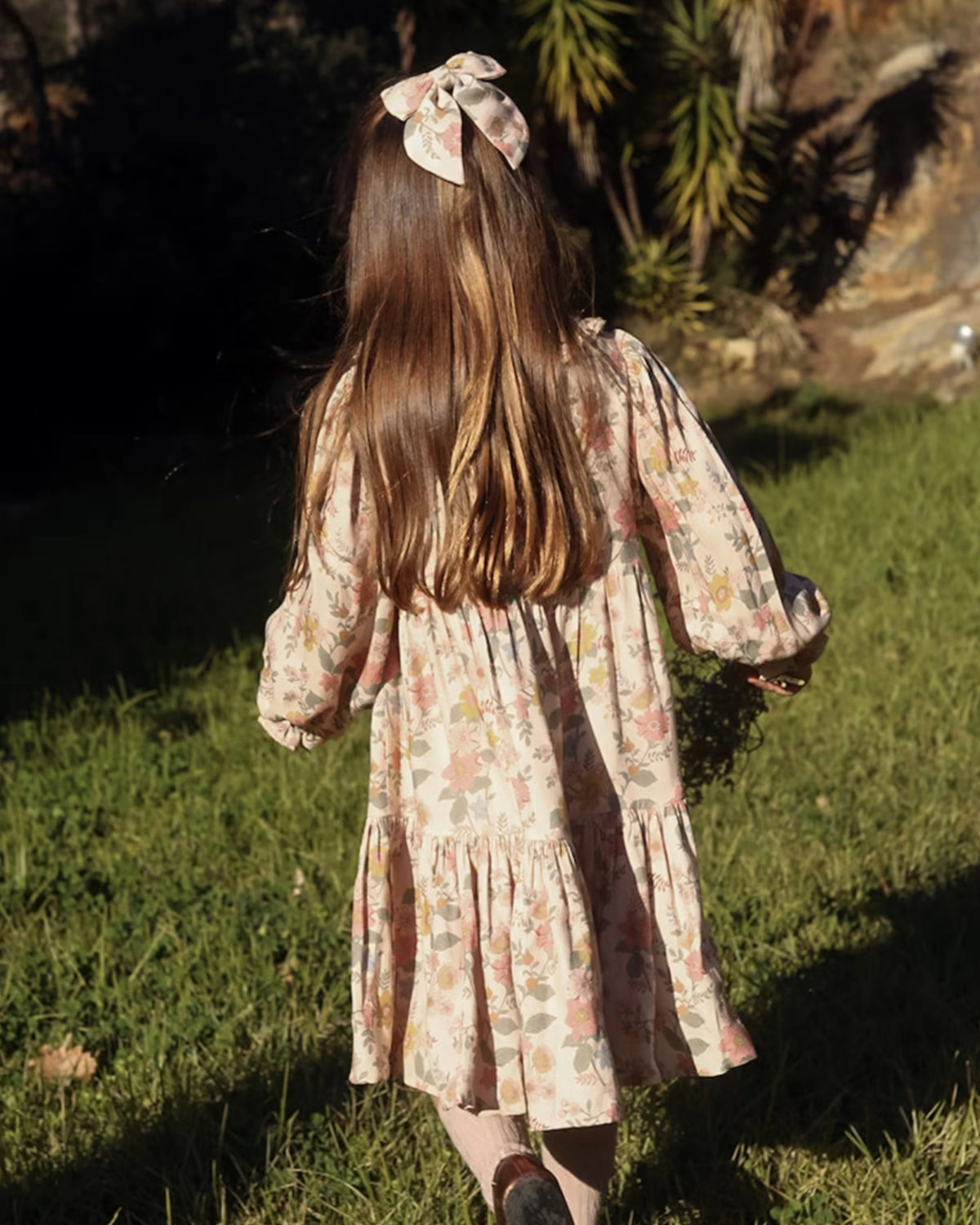 Early Sunday, Marguerite Dress in Bloom, made from Printed Viscose Twill fabric, featuring floral embroidery with frilled Peter Pan collar and gathered sleeves, shown in a back view of model wearing outdoors