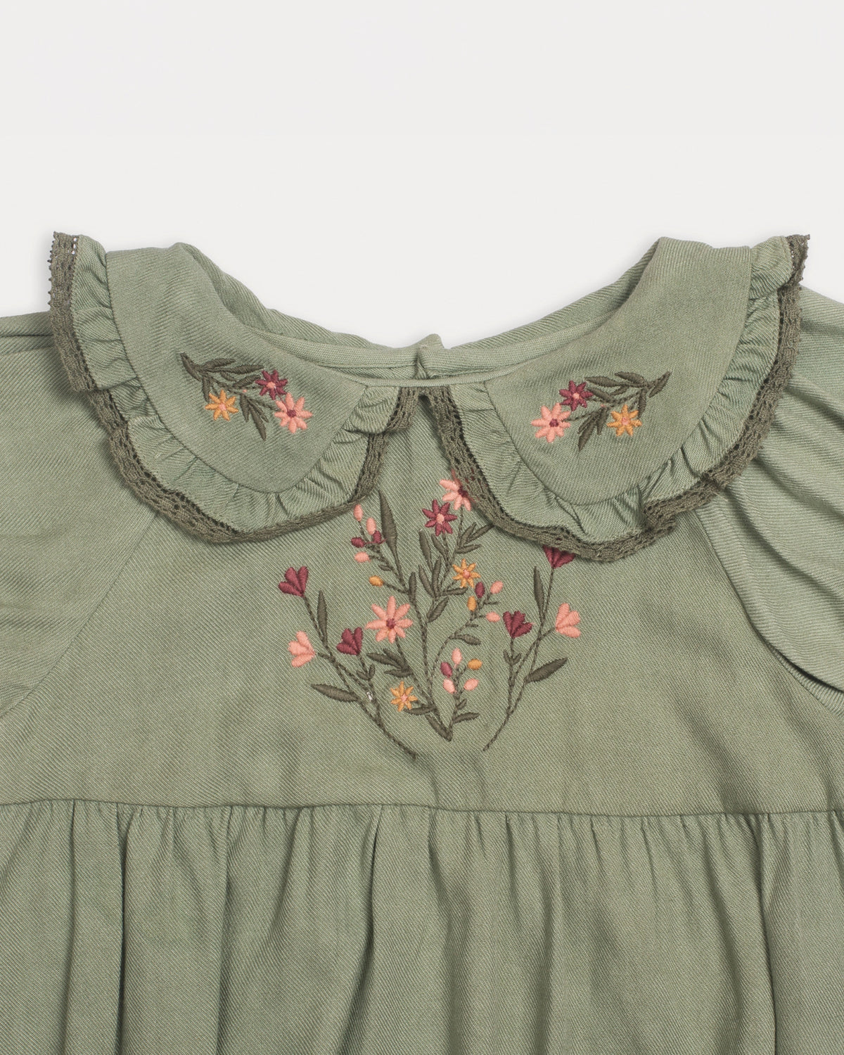Early Sunday, Mathilda Baby Bubble Romper in Sage Green, made from Viscose Twill fabric, featuring a floral embroidery on a frilly peter pan collar, shown in a closeup flat-lay view