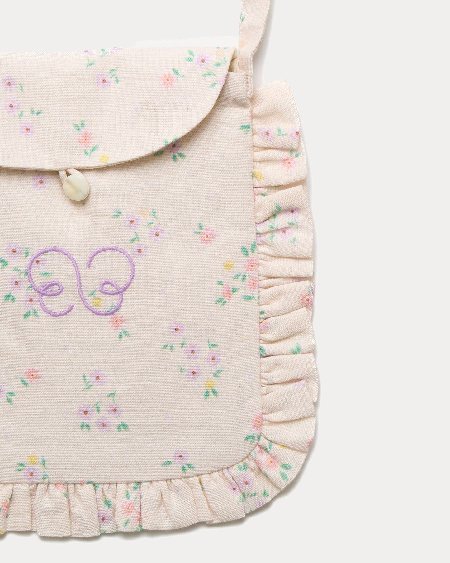 Early Sunday, Miss Sunday Sling in Painted Bouquet print, made from 70% Cotton, 30% Linen fabric, featuring a frill detailed sling purse with flap closure, shown in a closeup flat-lay view