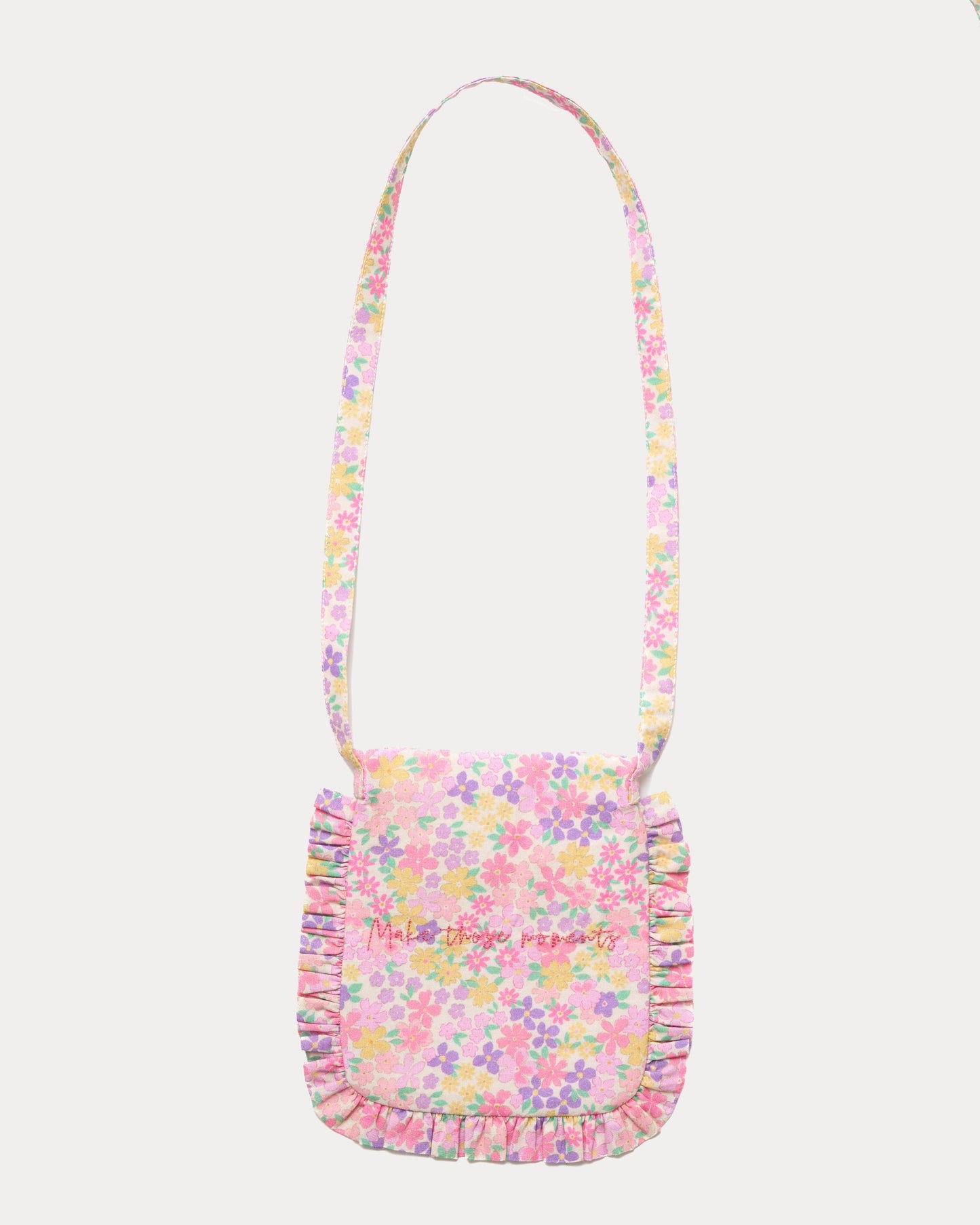 Early Sunday, Miss Sunday Sling in Emma Floral Purple color, made from Organic Printed Cotton Cambric fabric, featuring a frill detailed sling purse with flap closure, shown in back flat-lay view