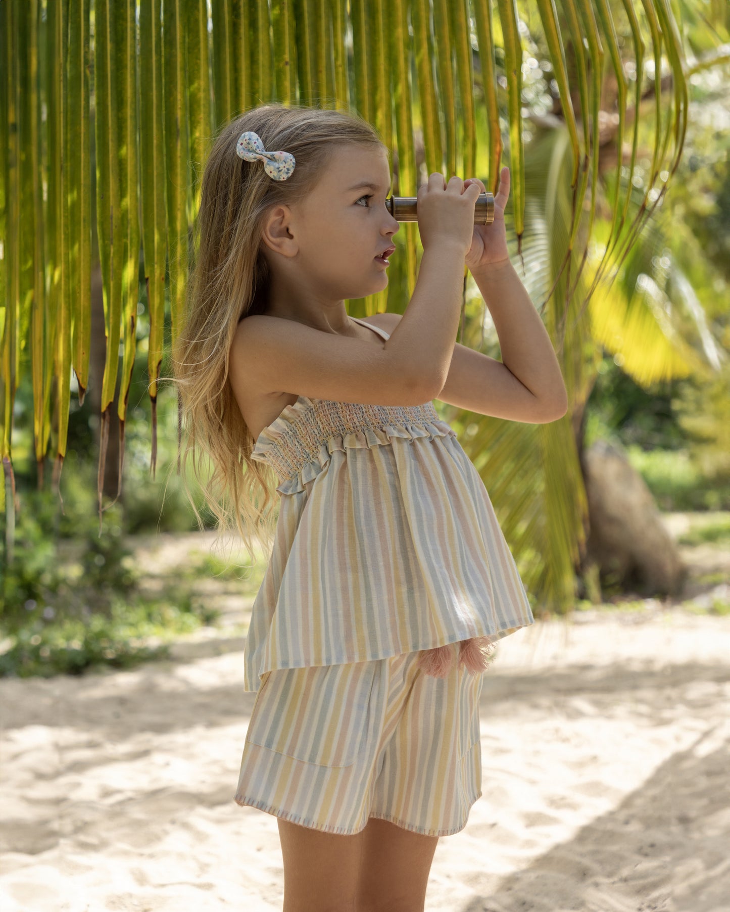 Early Sunday, Olivia Blouse in Summer Stripe, made from Printed canvas 70% Cotton 30% Linen fabric, featuring smocked bodice for a flexible fit, cross-back straps for added charm, and a flared hem for a breezy silhouette, shown in a outdoor shot of model wearing