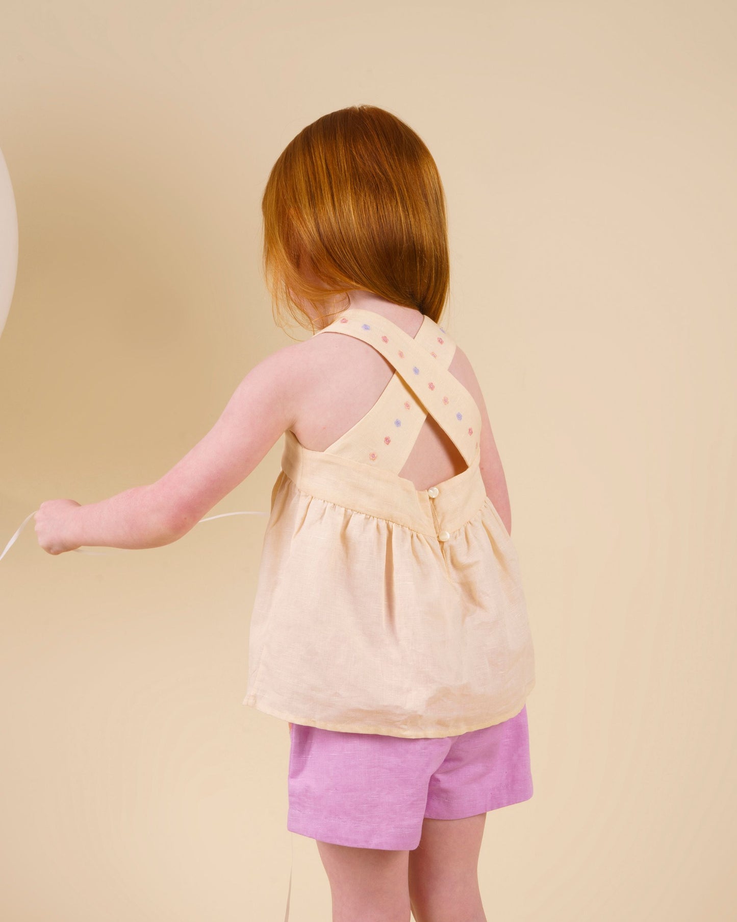 Early Sunday, Roman Short in Lilac color, made from 70% Cotton 30% Linen fabric, featuring a relaxed fit with an elastic waistband & beautiful embroidery, shown in a back view of a model wearing it in a studio setting