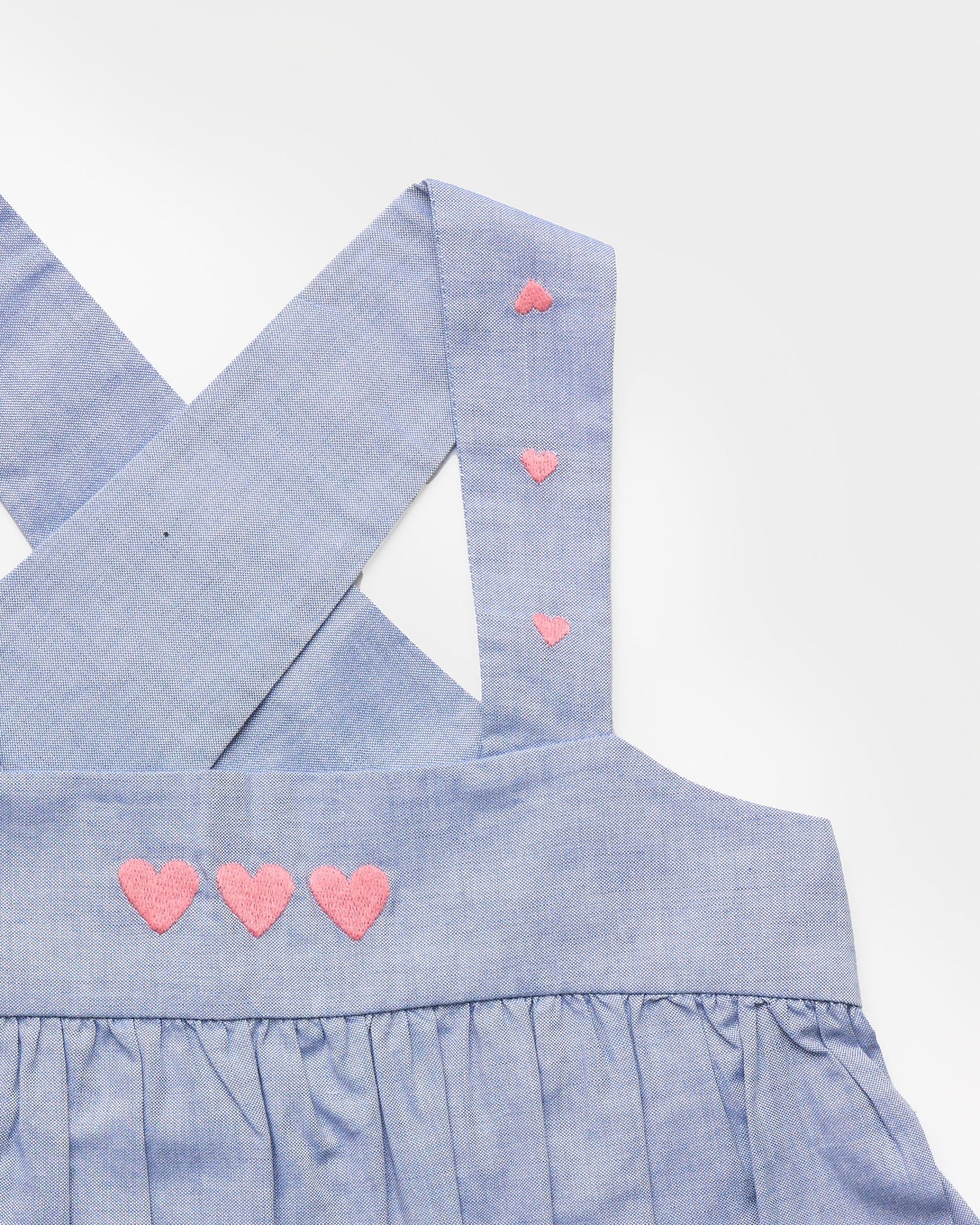 Early Sunday, Romy Blouse in Summer Sky color, made from 100% Cotton Chambray fabric, featuring a sleeveless design with cross-back straps, a gathered waist & a beautiful embroidery, shown in a closeup flat-lay view