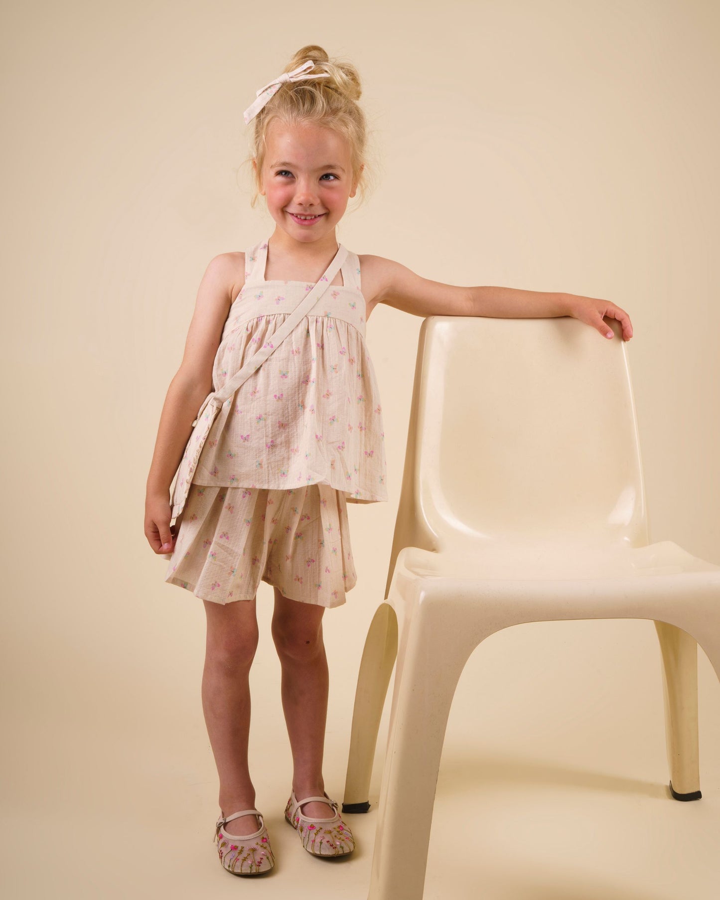 Early Sunday, Romy Blouse in Butterflies print, made from Printed Cotton Tiny Swiss Dobby fabric, featuring a sleeveless design with cross-back straps, a gathered waist & a soft flared silhouette, shown in front view of a model wearing it in a studio setting
