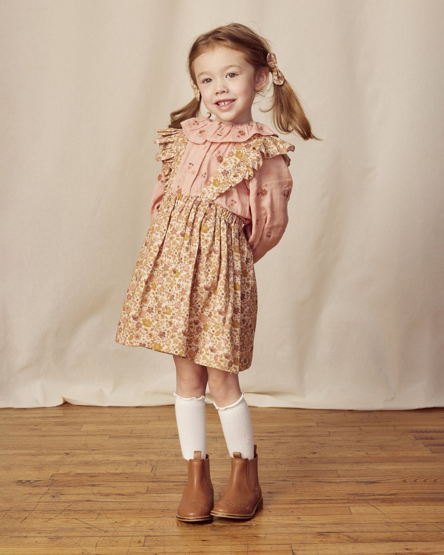 Early Sunday, Selma Skirt in Garden Flowers Dusty Pink, made from Printed Cotton Satin fabric, featuring dungaree style with adjustable straps, shown in a front view of a model wearing it in a studio setting