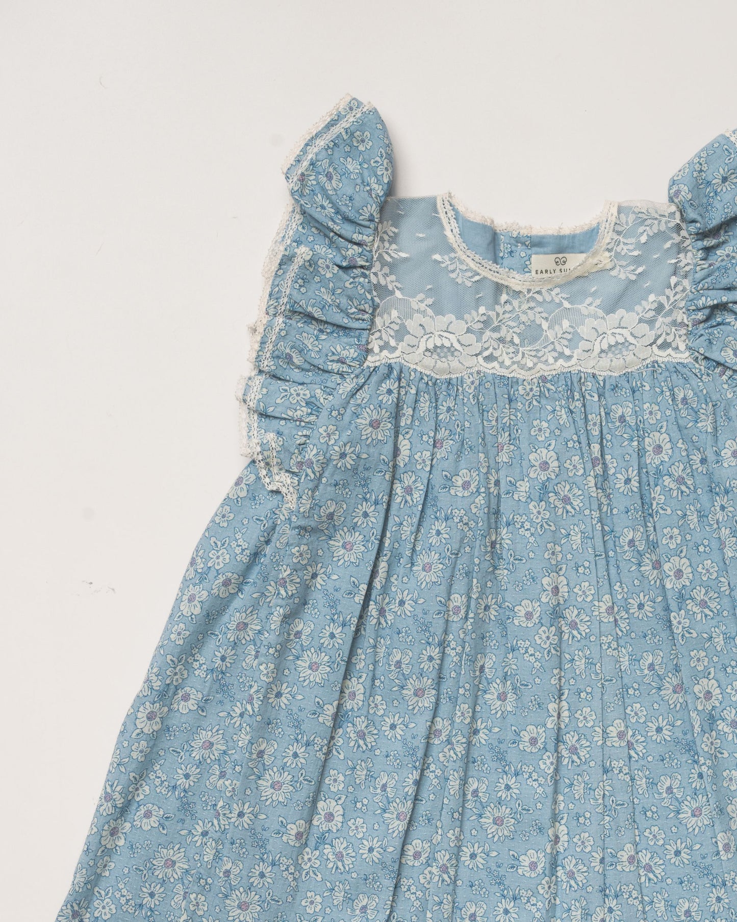 Early Sunday, Sita Dress in Tonal Floral Blue color, made from Printed Cotton Tiny Swiss Dobby fabric, featuring a sleeveless design with wide shoulder straps & a delicate lace yoke, shown in a closeup flat-lay view