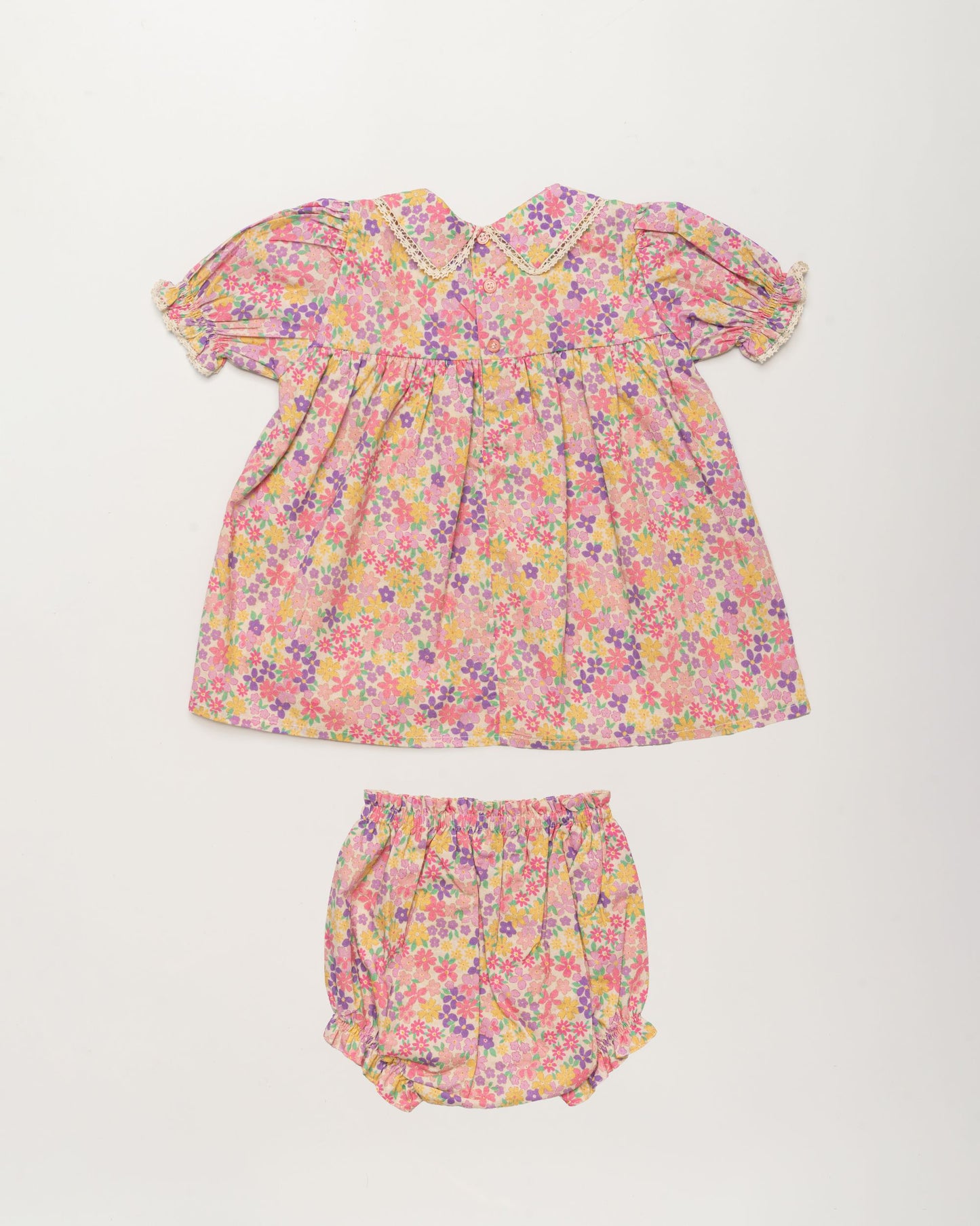 Early Sunday, Sofia Baby Dress & Bloomer Set in Emma Floral Purple color, made from 100% Organic Cotton 60s Cambric fabric, featuring short sleeves with peter pan collar, shown in a back flat-lay view