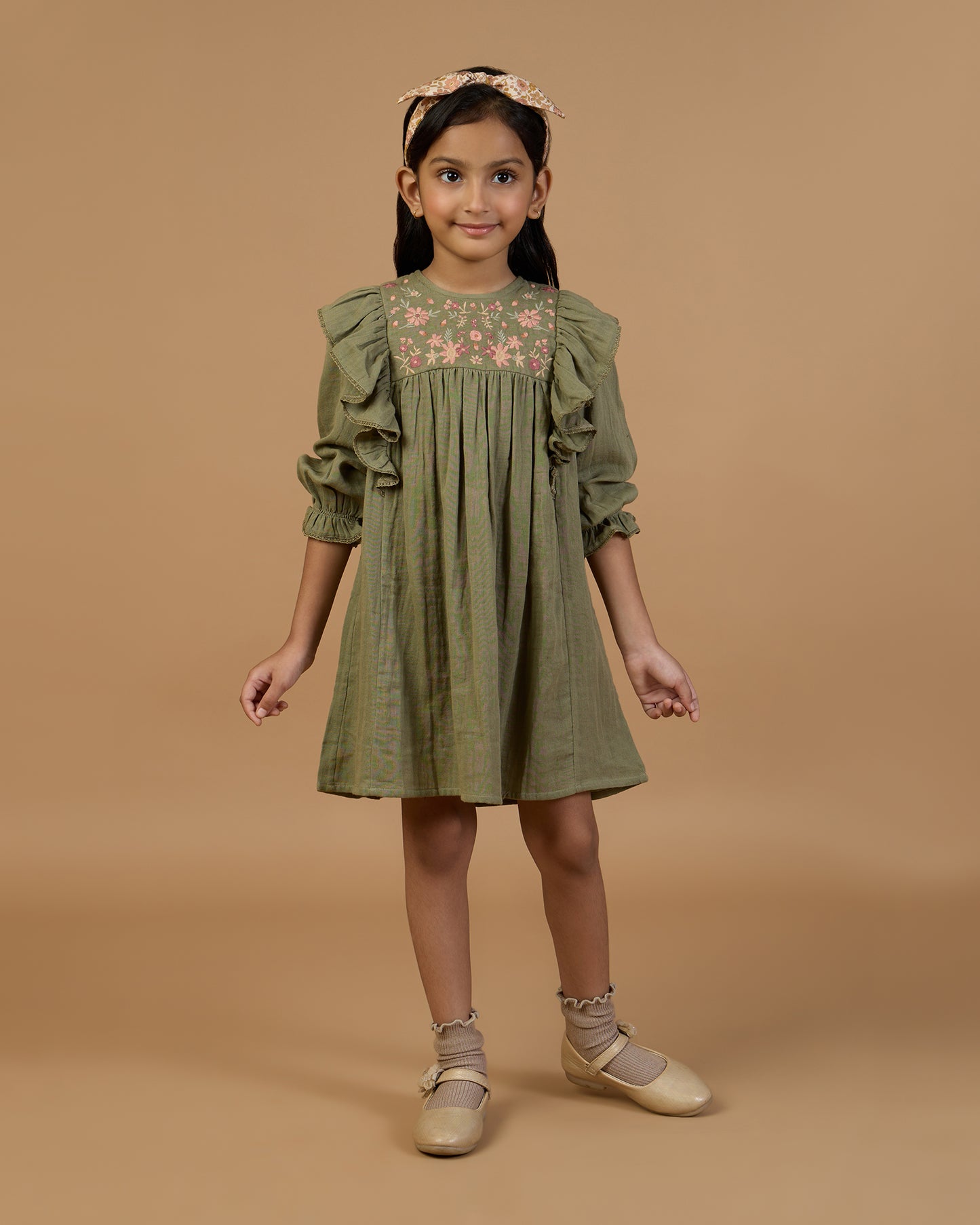 Early Sunday, Suzanne Dress in Dried Leaf, made from Cotton Double Gauze fabric, featuring classic silhouette with floral embroidery around the yoke and ruffle detailing, shown in a front view of a model wearing it in a studio setting