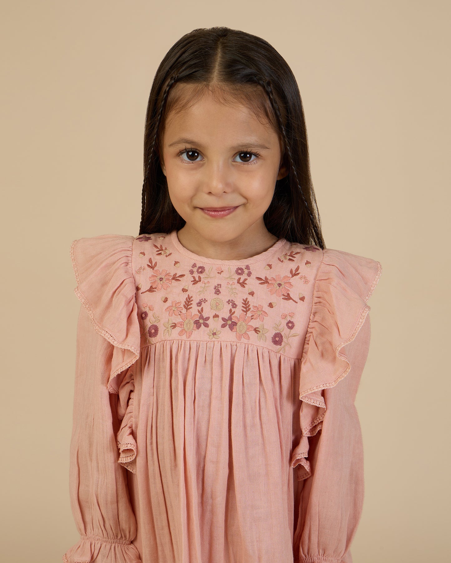 Early Sunday, Suzanne Dress in Dusty Pink, made from Cotton Double Gauze fabric, featuring classic silhouette with floral embroidery around the yoke and ruffle detailing, shown in a close-up shot of a model wearing it during a studio shoot