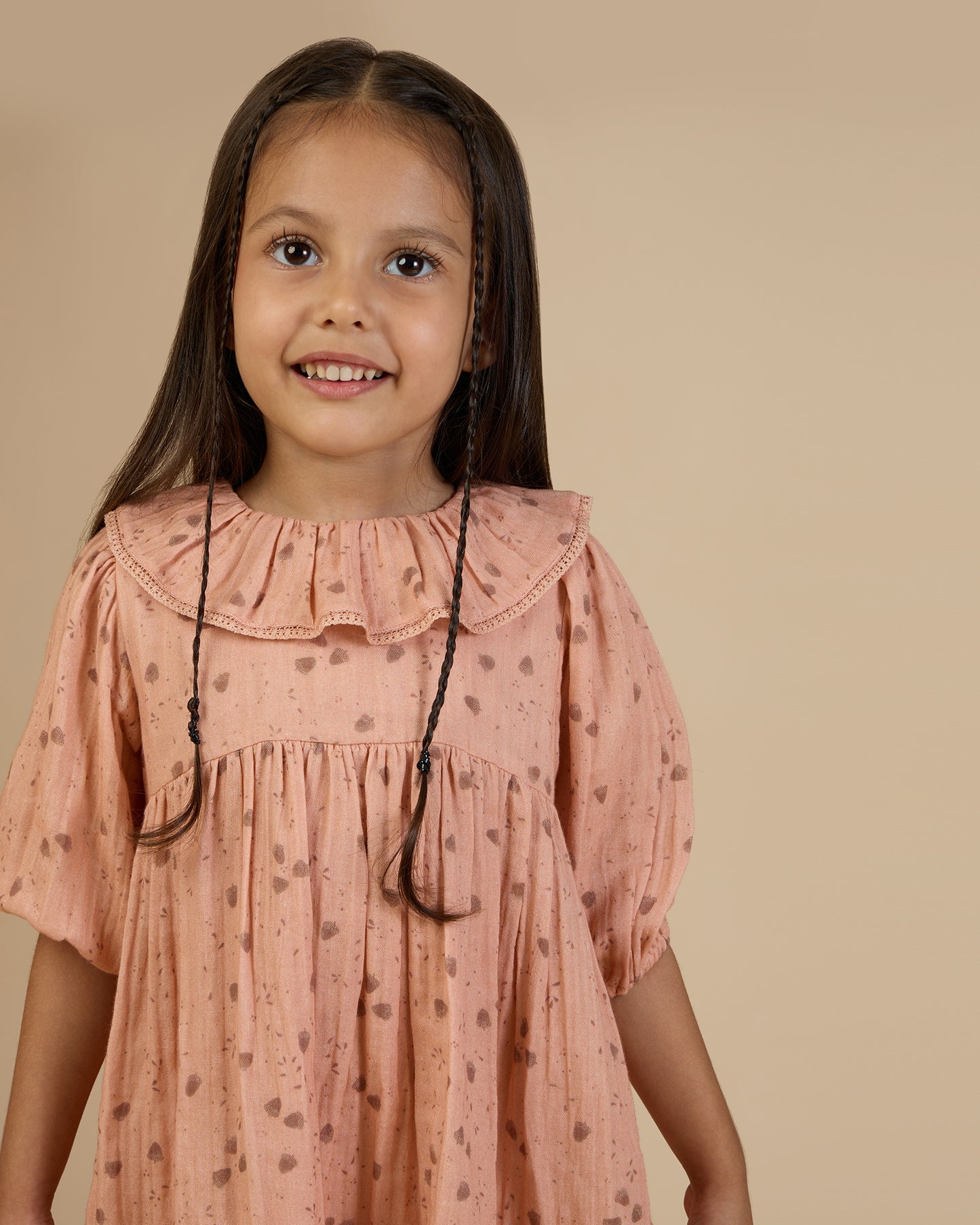 Early Sunday, Suzie Dress in Acorn Dusty Pink, made from Printed Cotton Double Gauze fabric, featuring classic silhouette with a ruffle neckline and mother-of-pearl buttons, shown in a close-up shot of a model wearing it during a studio shoot