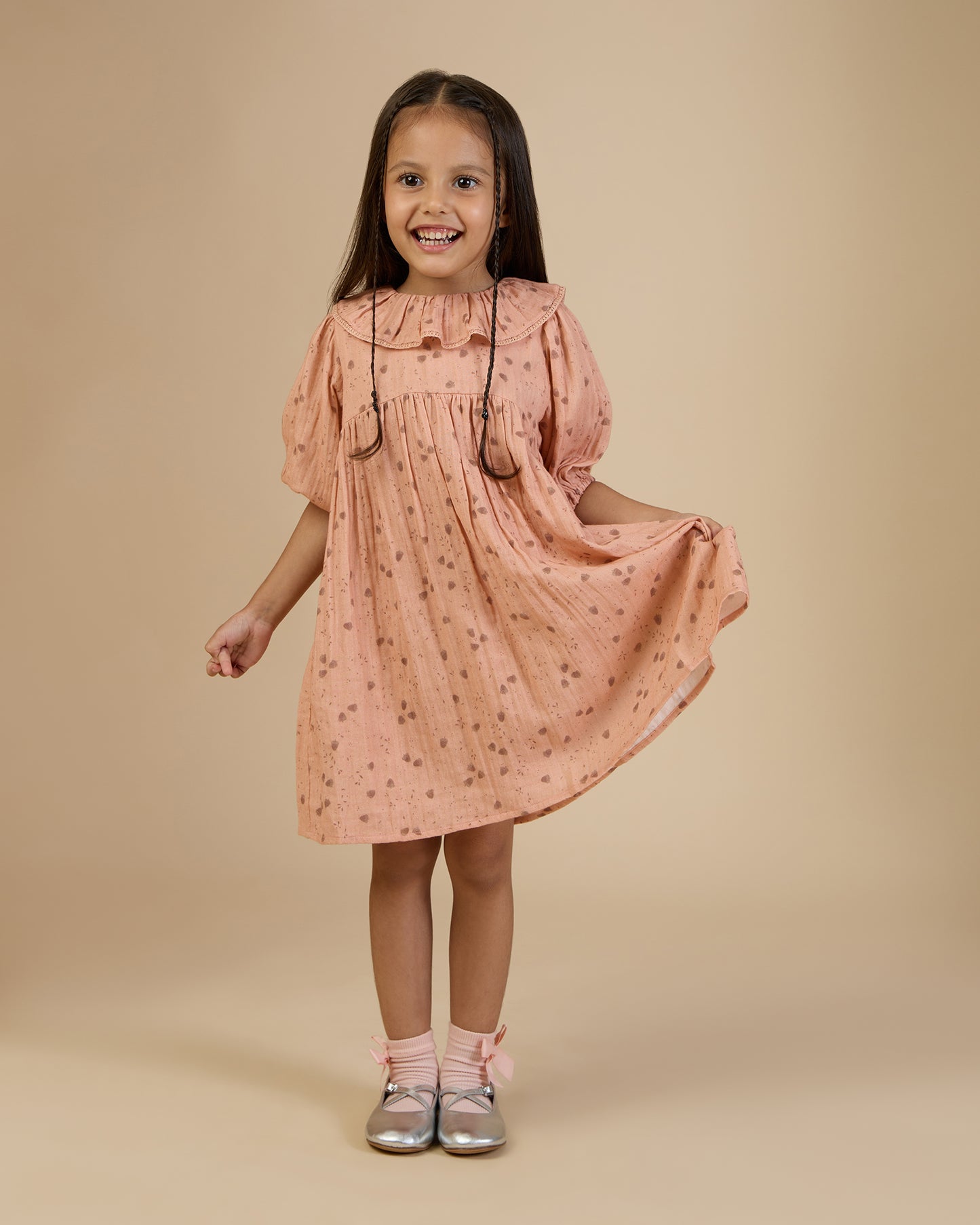Early Sunday, Suzie Dress in Acorn Dusty Pink, made from Printed Cotton Double Gauze fabric, featuring classic silhouette with a ruffle neckline and mother-of-pearl buttons, shown in a front view of a model wearing it in a studio setting