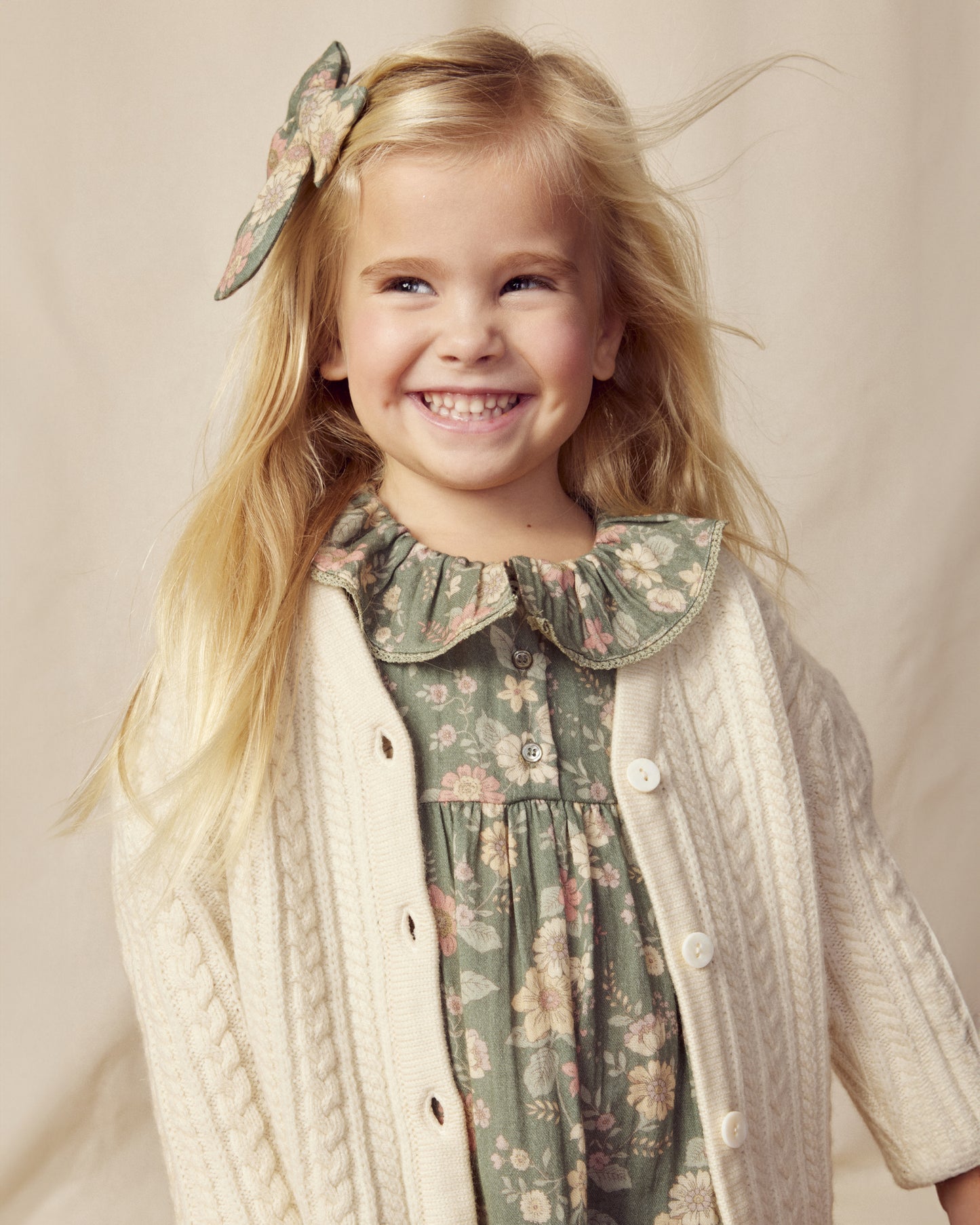 Early Sunday, Suzie Dress in Autumn Bloom Soft Green, made from Printed Cotton Double Gauze fabric, featuring classic silhouette with a ruffle neckline and mother-of-pearl buttons, shown in a close-up shot of a model wearing it during a studio shoot