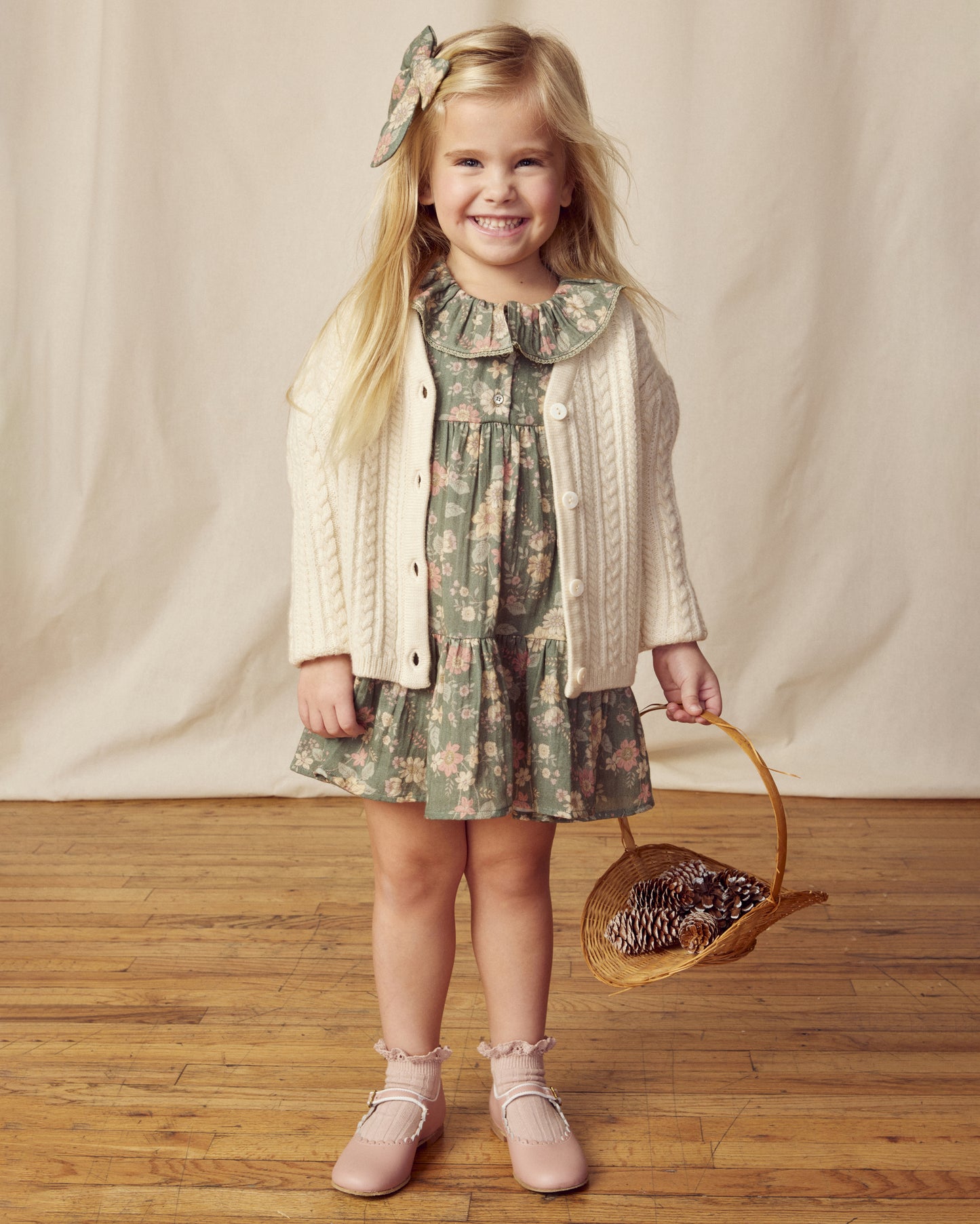Early Sunday, Suzie Dress in Autumn Bloom Soft Green, made from Printed Cotton Double Gauze fabric, featuring classic silhouette with a ruffle neckline and mother-of-pearl buttons, shown in a front view of a model wearing it in a studio setting