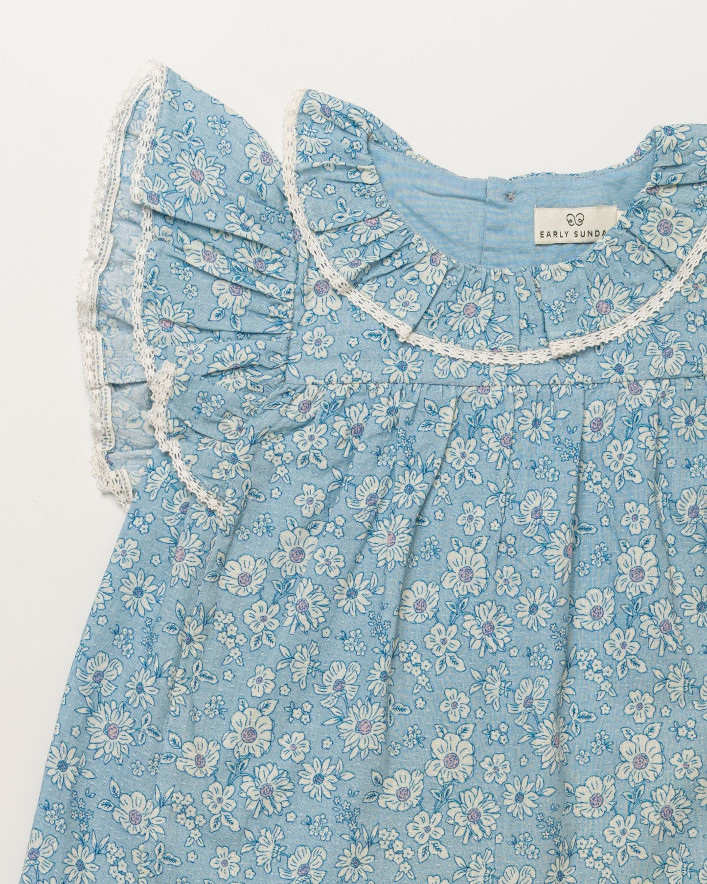 Early Sunday, Vicky Baby Dress & Bloomer Set in Tonal Floral Blue color, made from 100% Cotton Swiss Dobby Tiny Dots fabric, featuring a floral print with lace borders, shown in a closeup flat-lay view