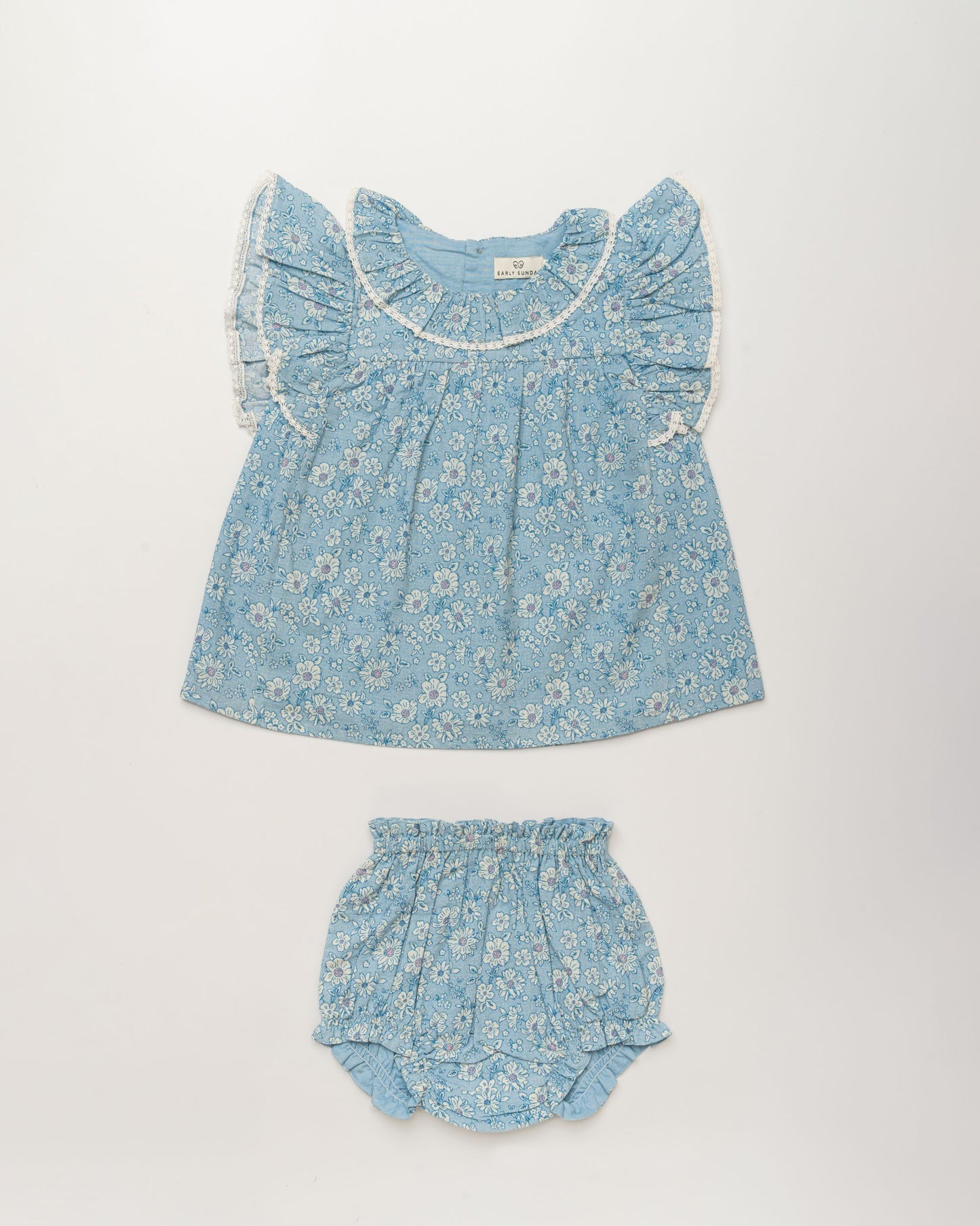 Early Sunday, Vicky Baby Dress & Bloomer Set in Tonal Floral Blue color, made from 100% Cotton Swiss Dobby Tiny Dots fabric, featuring a floral print with lace borders, shown in a front flat-lay view