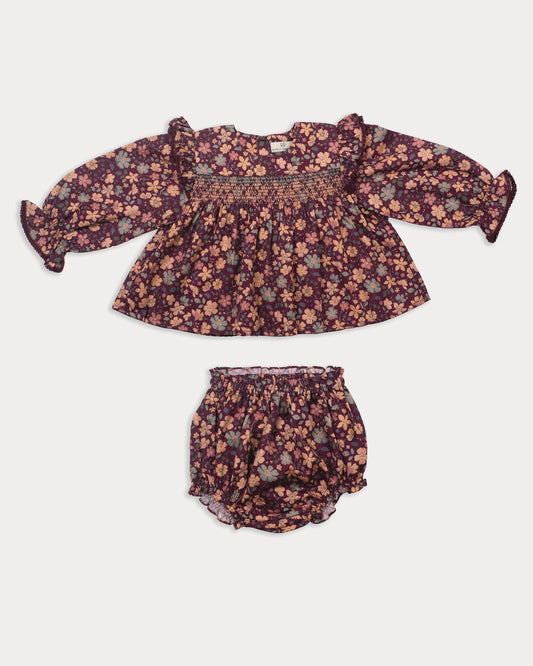 Early Sunday, Ellie Baby Dress & Bloomer Set in Garden Flowers Plum, made from Printed Cotton Satin fabric, featuring frilly sleeves across shoulder & smocked chest, shown in a front flat-lay view