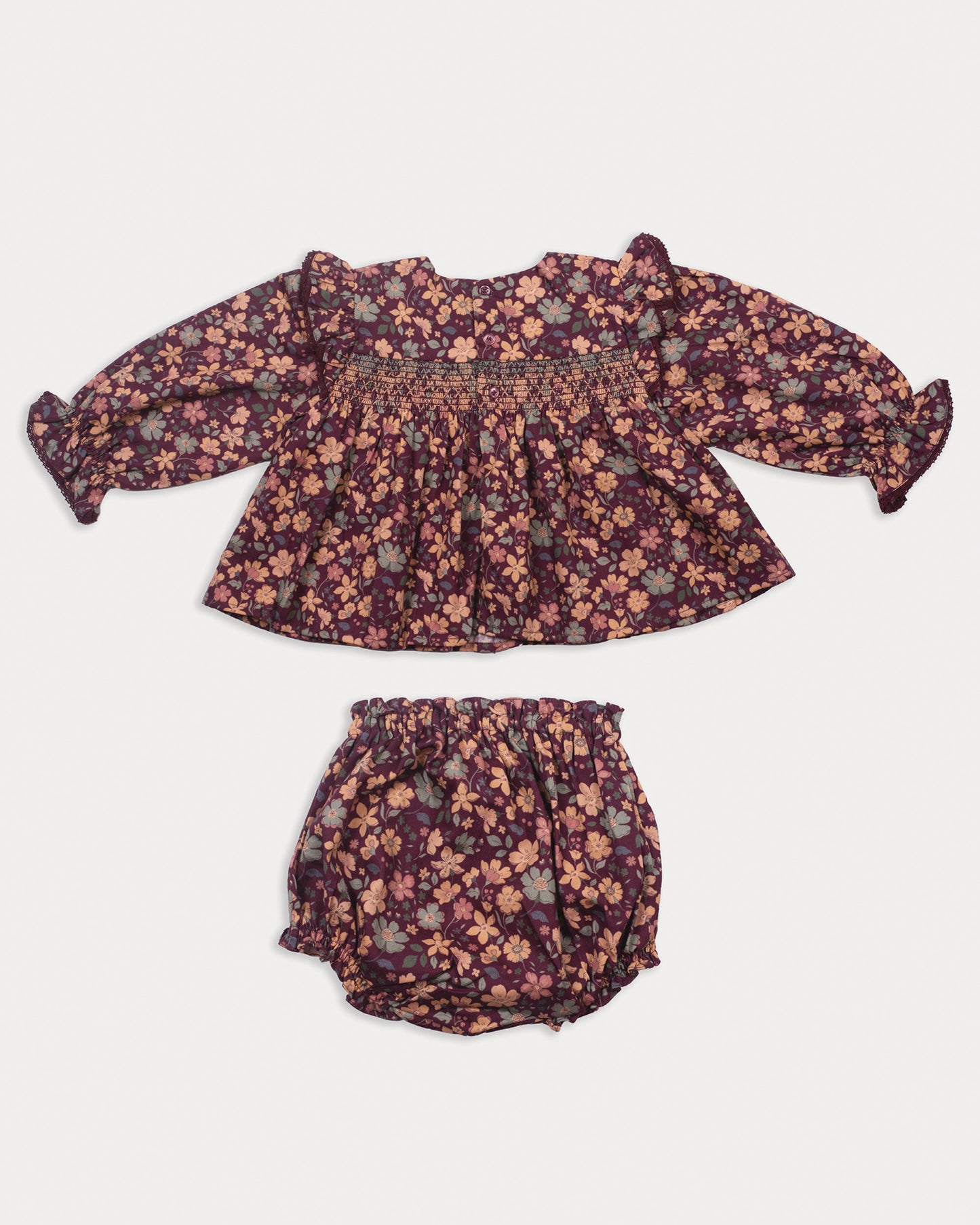 Early Sunday, Ellie Baby Dress & Bloomer Set in Garden Flowers Plum, made from Printed Cotton Satin fabric, featuring frilly sleeves across shoulder & smocked chest, shown in a back flat-lay view