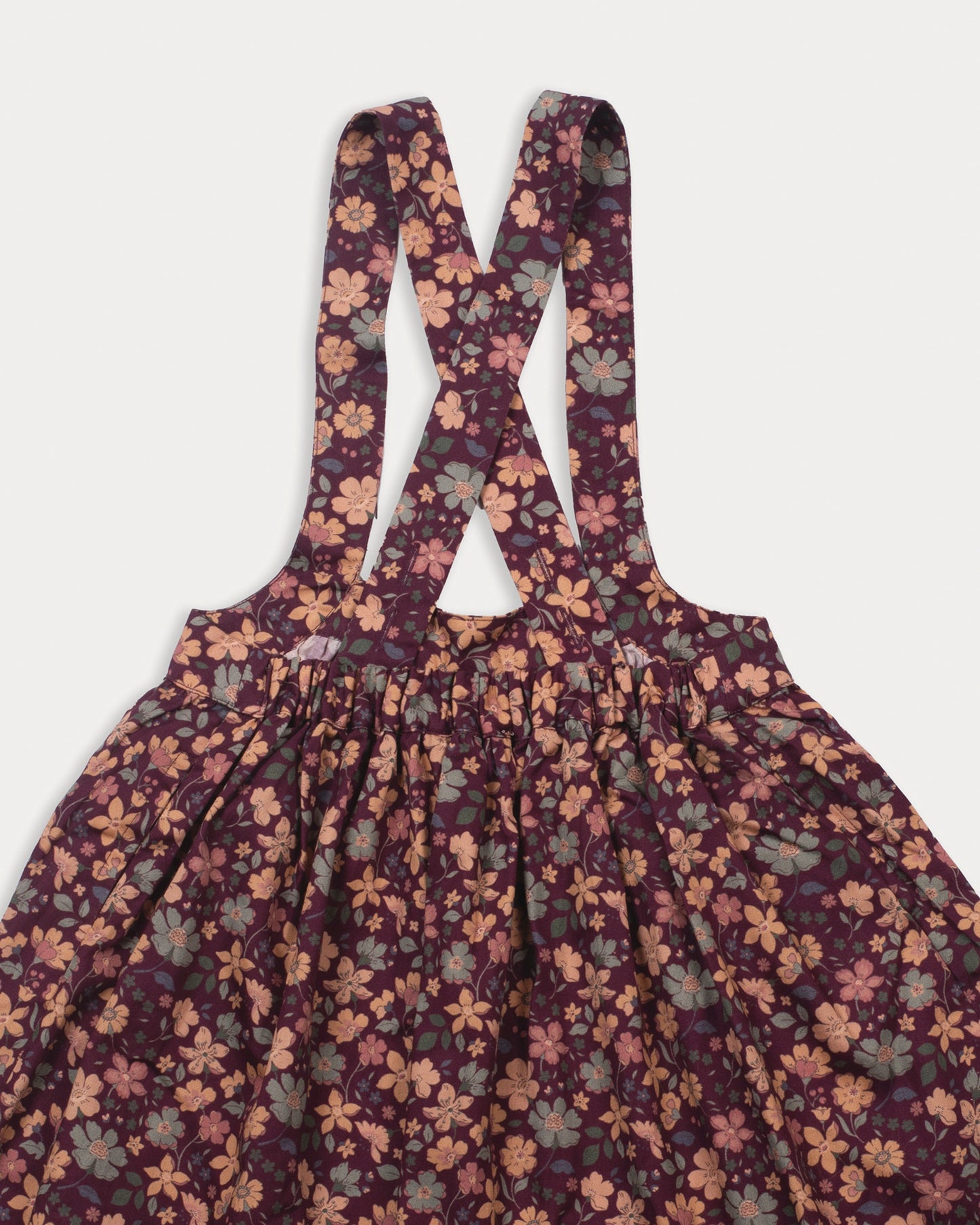 Early Sunday, Annie Skirt in Garden Flowers Plum, made from Printed Cotton Satin fabric, featuring an A-line silhouette with adjustable cross-back straps and soft gathers, shown in a closeup flat-lay view