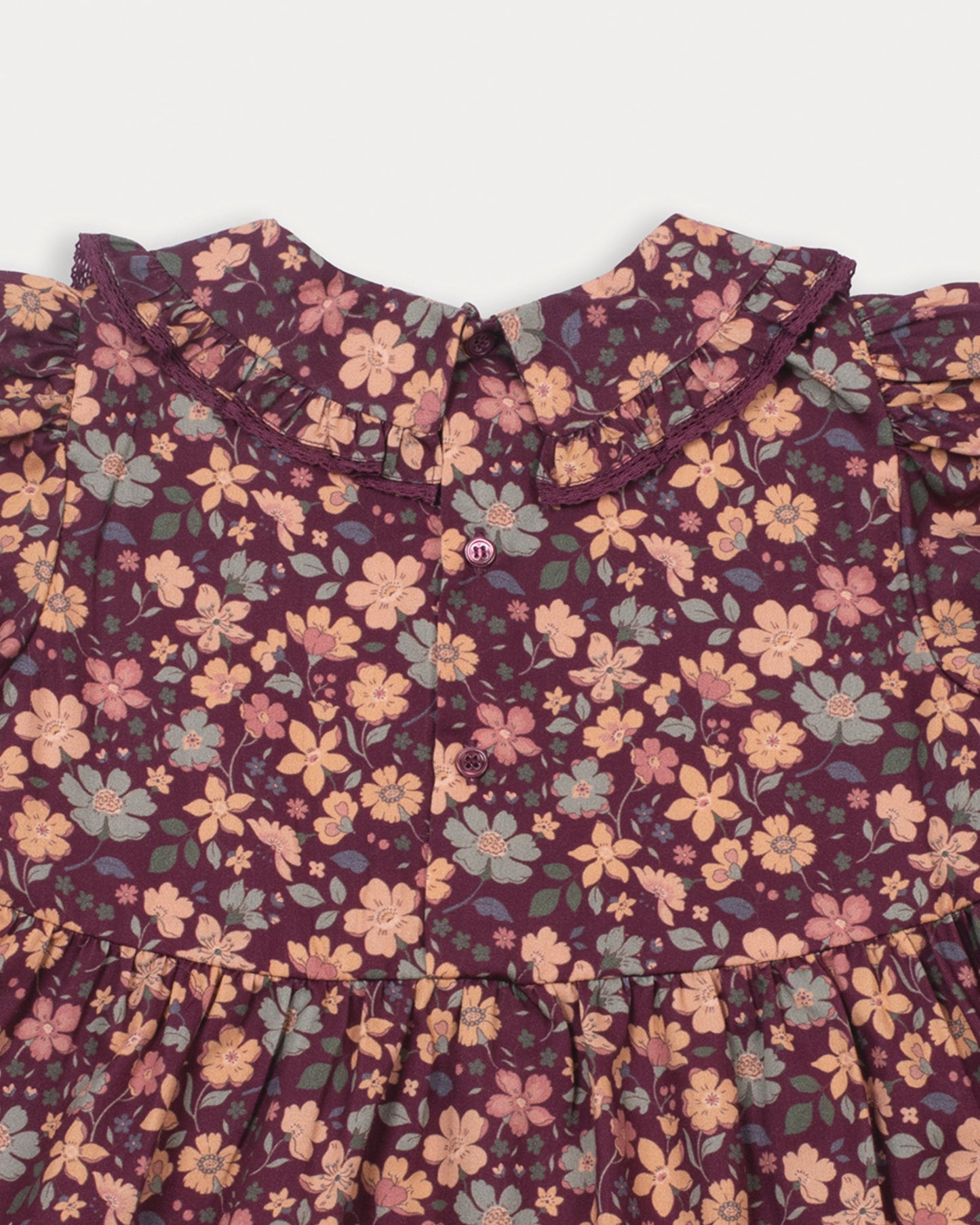 Early Sunday, Marguerite Dress in Garden Flowers Plum, made from Printed Cotton Satin fabric, featuring floral print and detailed lace yoke with Peter Pan collar, shown in a closeup flat-lay view