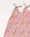 Early Sunday, Alena dress in Emma Floral Purple color, made from organic printed cotton cambric fabric, featuring tie-up shoulder straps, gathered flare, and ruffled hem, shown in a closeup flat-lay view.