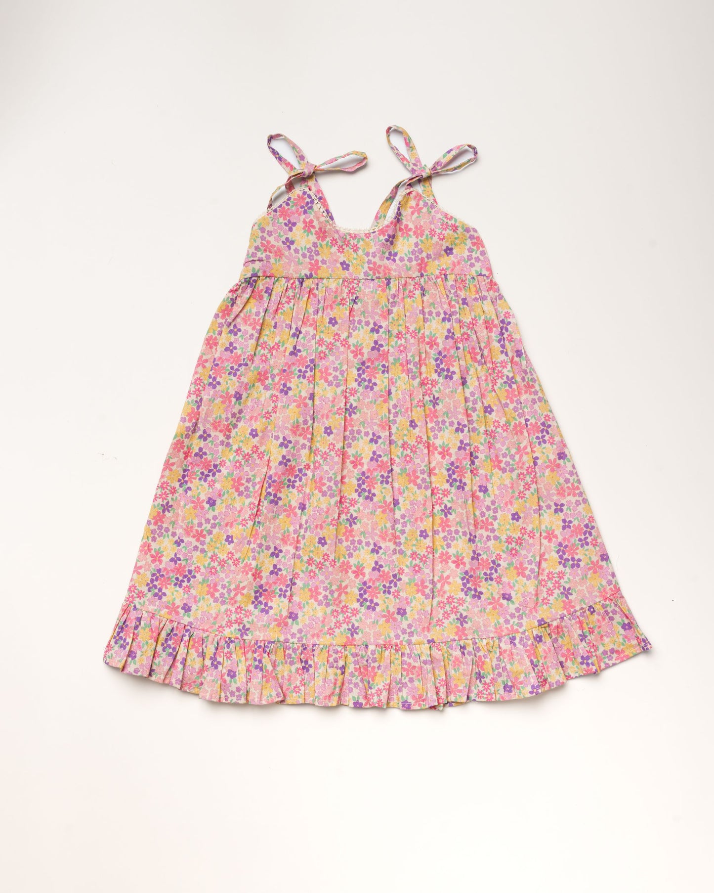 Early Sunday, Alena dress in Emma Floral Purple color, made from organic printed cotton cambric fabric, featuring tie-up shoulder straps, gathered flare, and ruffled hem, shown in a front flat-lay view.