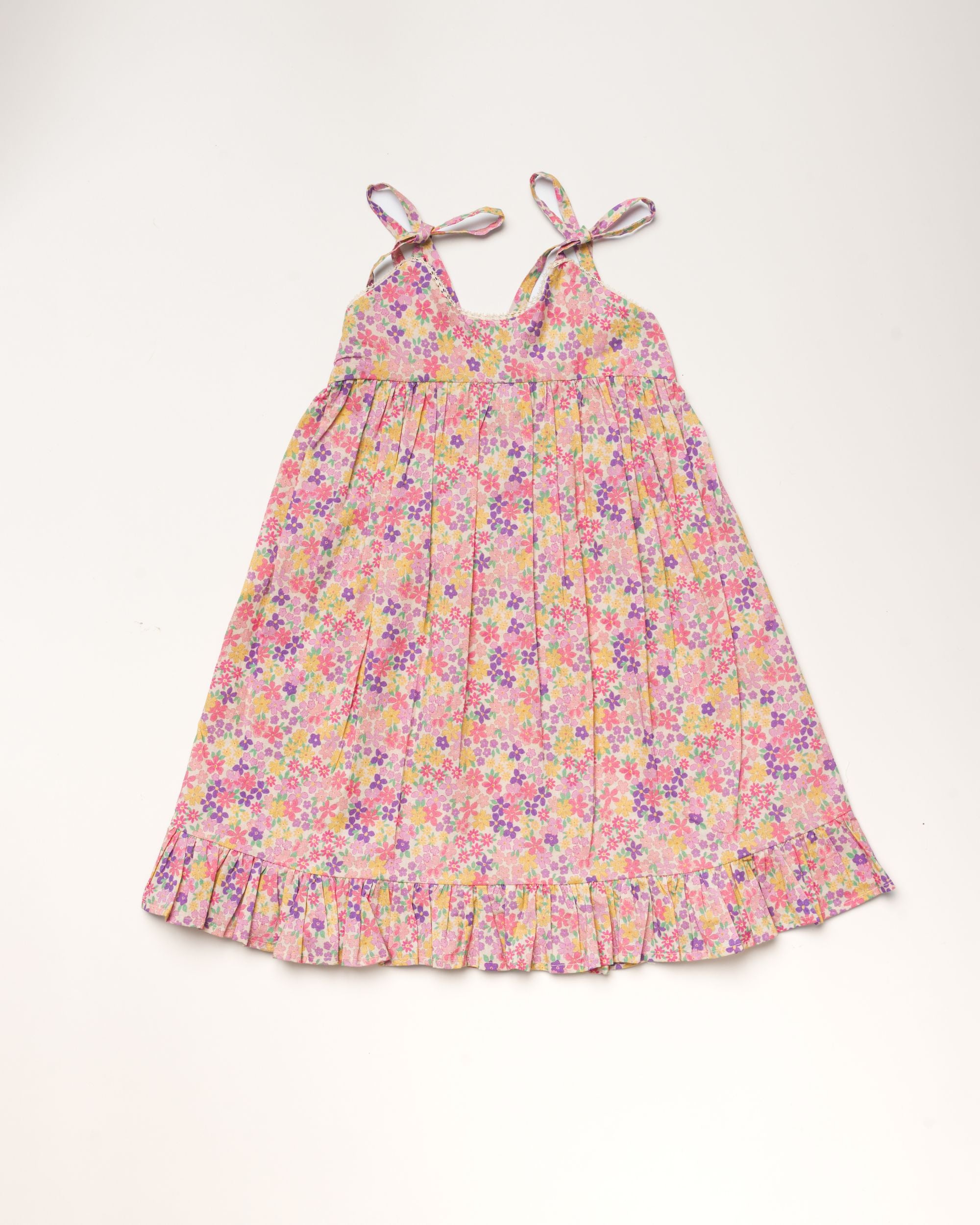 Early Sunday, Alena dress in Emma Floral Purple color, made from organic printed cotton cambric fabric, featuring tie-up shoulder straps, gathered flare, and ruffled hem, shown in a front flat-lay view.