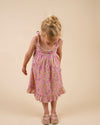 Early Sunday, Alena dress in Emma Floral Purple color, made from organic printed cotton cambric fabric, featuring tie-up shoulder straps, gathered flare, and ruffled hem, shown in a front view of model wearing it.