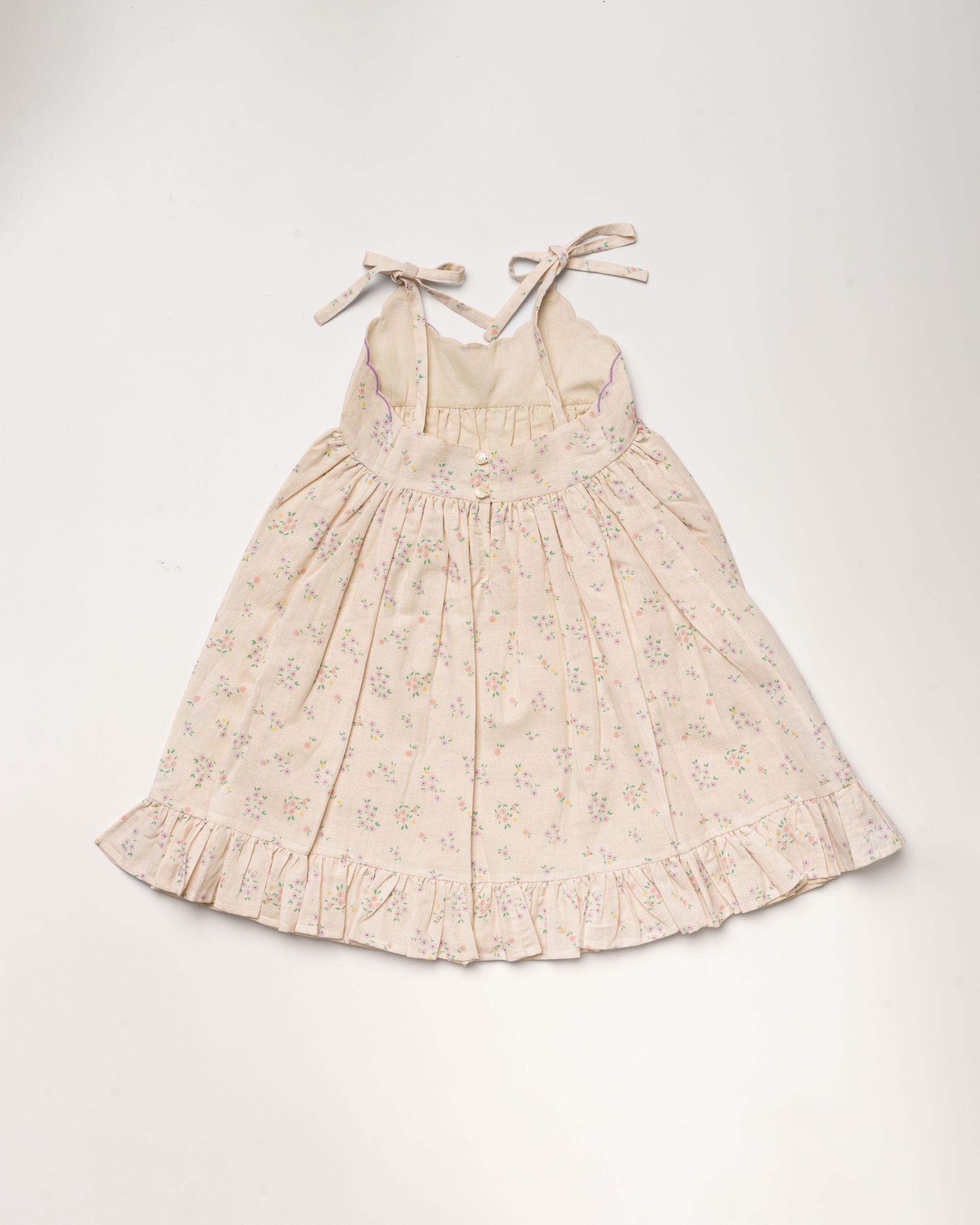 Early Sunday, Alena dress in Painted Bouquet color, made from printed 70% cotton 30% linen fabric, featuring tie-up shoulder straps, gathered flare, and ruffled hem, shown in a back flat-lay view.