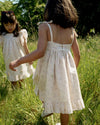 Early Sunday, Alena dress in Painted Bouquet color, made from printed 70% cotton 30% linen fabric, featuring tie-up shoulder straps, gathered flare, and ruffled hem, shown in a back view of model wearing it.