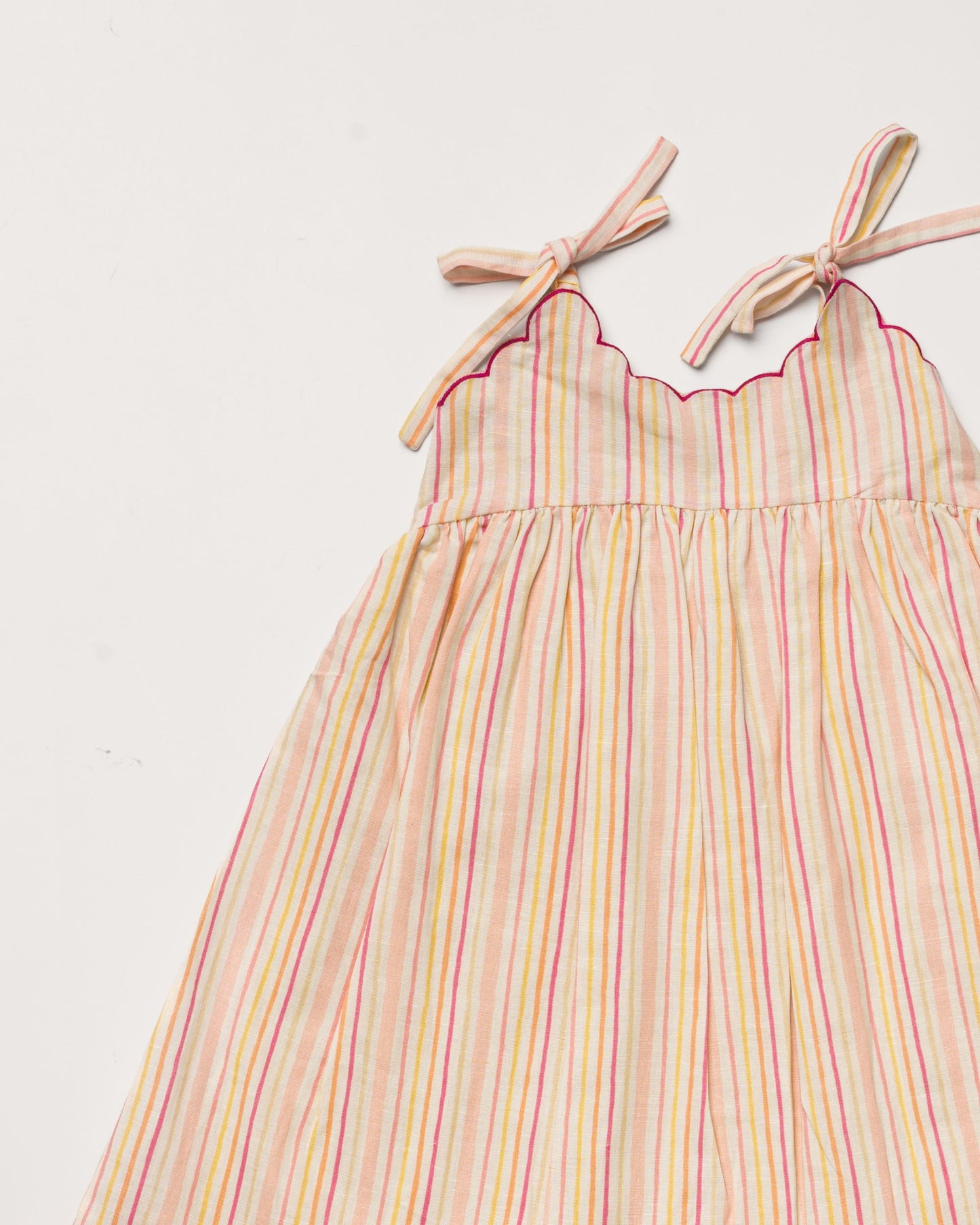 Early Sunday, Alena dress in Pink Stripes color, made from printed 70% cotton 30% linen fabric, featuring tie-up shoulder straps, gathered flare, and ruffled hem, shown in a closeup flat-lay view.