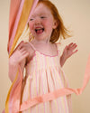 Early Sunday, Alena dress in Pink Stripes color, made from printed 70% cotton 30% linen fabric, featuring tie-up shoulder straps, gathered flare, and ruffled hem, shown in a model in motion.