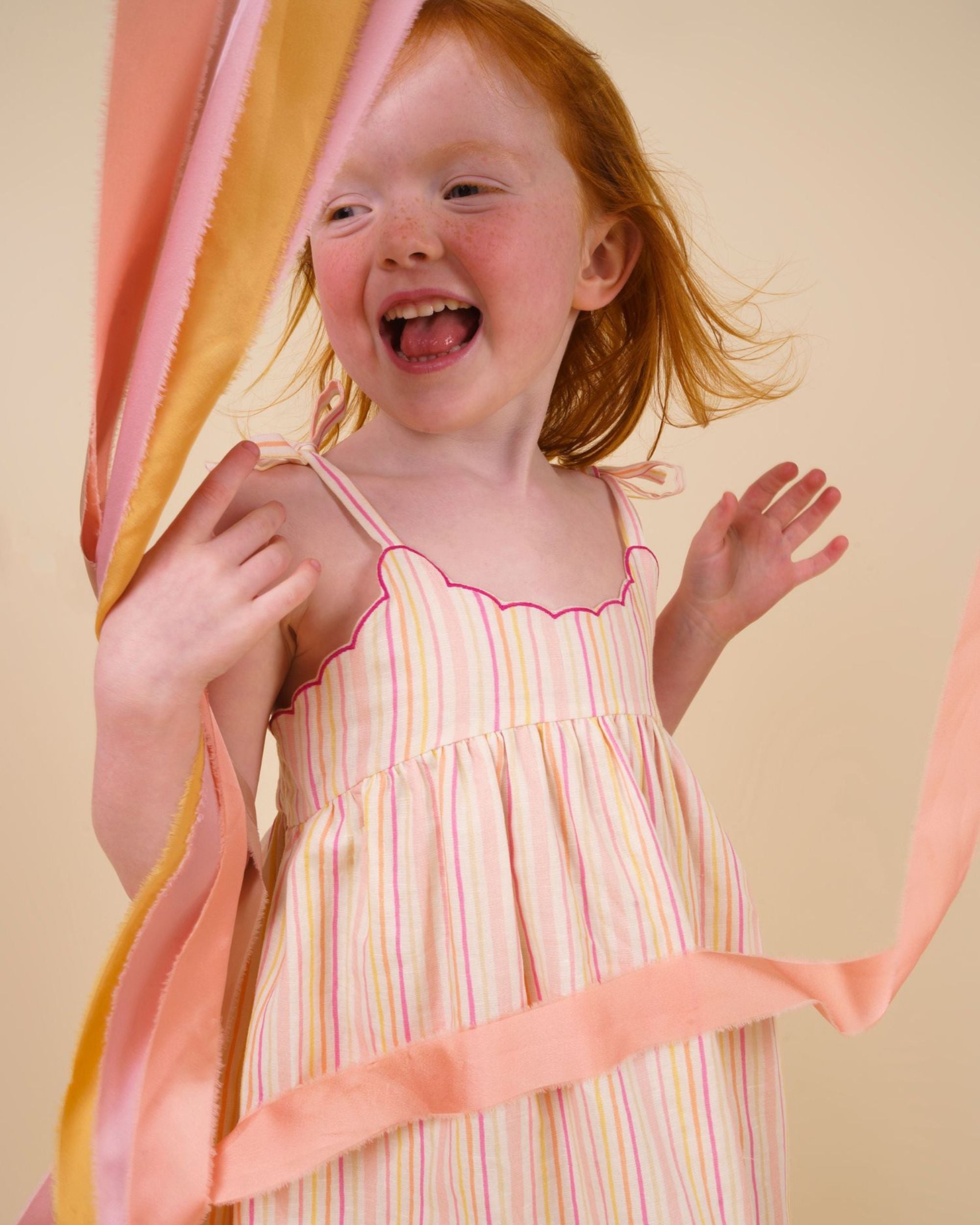Early Sunday, Alena dress in Pink Stripes color, made from printed 70% cotton 30% linen fabric, featuring tie-up shoulder straps, gathered flare, and ruffled hem, shown in a model in motion.