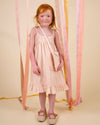 Early Sunday, Alena dress in Pink Stripes color, made from printed 70% cotton 30% linen fabric, featuring tie-up shoulder straps, gathered flare, and ruffled hem, shown in a front view of model wearing.
