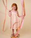 Early Sunday, Alena dress in Pink Stripes color, made from printed 70% cotton 30% linen fabric, featuring tie-up shoulder straps, gathered flare, and ruffled hem, shown in a model in motion.