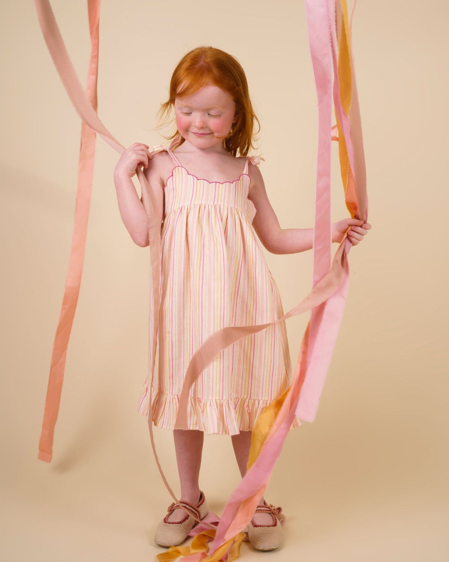 Early Sunday, Alena dress in Pink Stripes color, made from printed 70% cotton 30% linen fabric, featuring tie-up shoulder straps, gathered flare, and ruffled hem, shown in a model in motion.