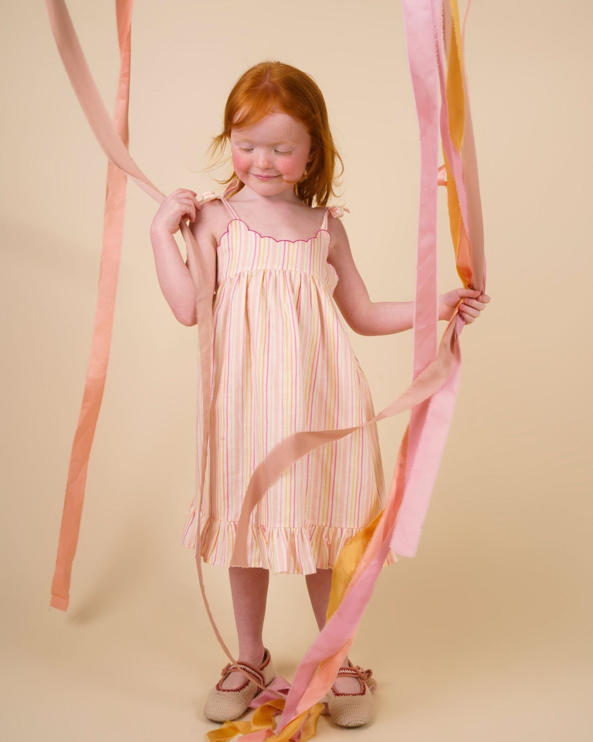 Early Sunday, Alena dress in Pink Stripes color, made from printed 70% cotton 30% linen fabric, featuring tie-up shoulder straps, gathered flare, and ruffled hem, shown in a model in motion.
