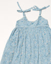 Early Sunday, Alena dress in Tonal Floral Blue color, made from printed cotton tiny swiss dobby fabric, featuring tie-up shoulder straps, gathered flare, and ruffled hem, shown in a closeup flat-lay view.