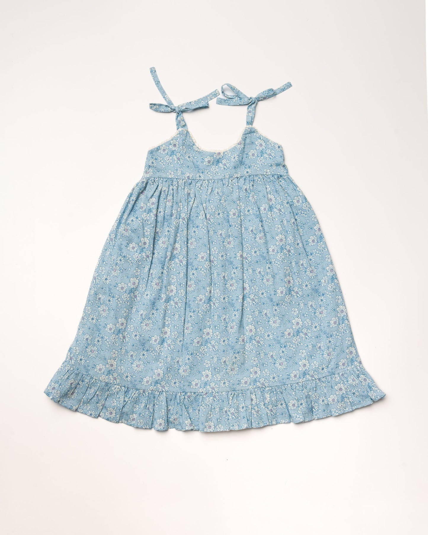 Early Sunday, Alena dress in Tonal Floral Blue color, made from printed cotton tiny swiss dobby fabric, featuring tie-up shoulder straps, gathered flare, and ruffled hem, shown in a front flat-lay view.